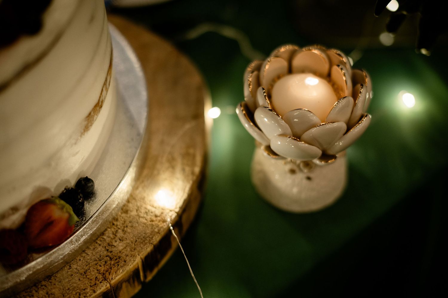 A delicate vintage candle holder with a flower-shaped design glows softly against a dark green background.