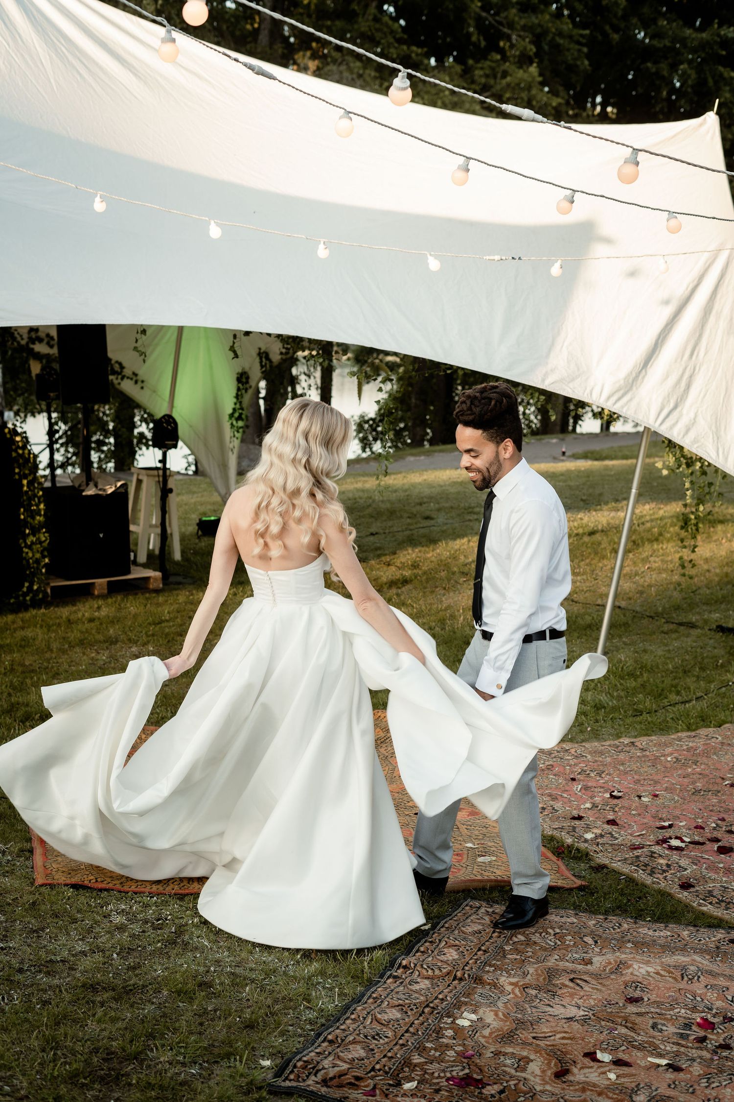 Couple dancing under white tent with string lights at outdoor wedding.