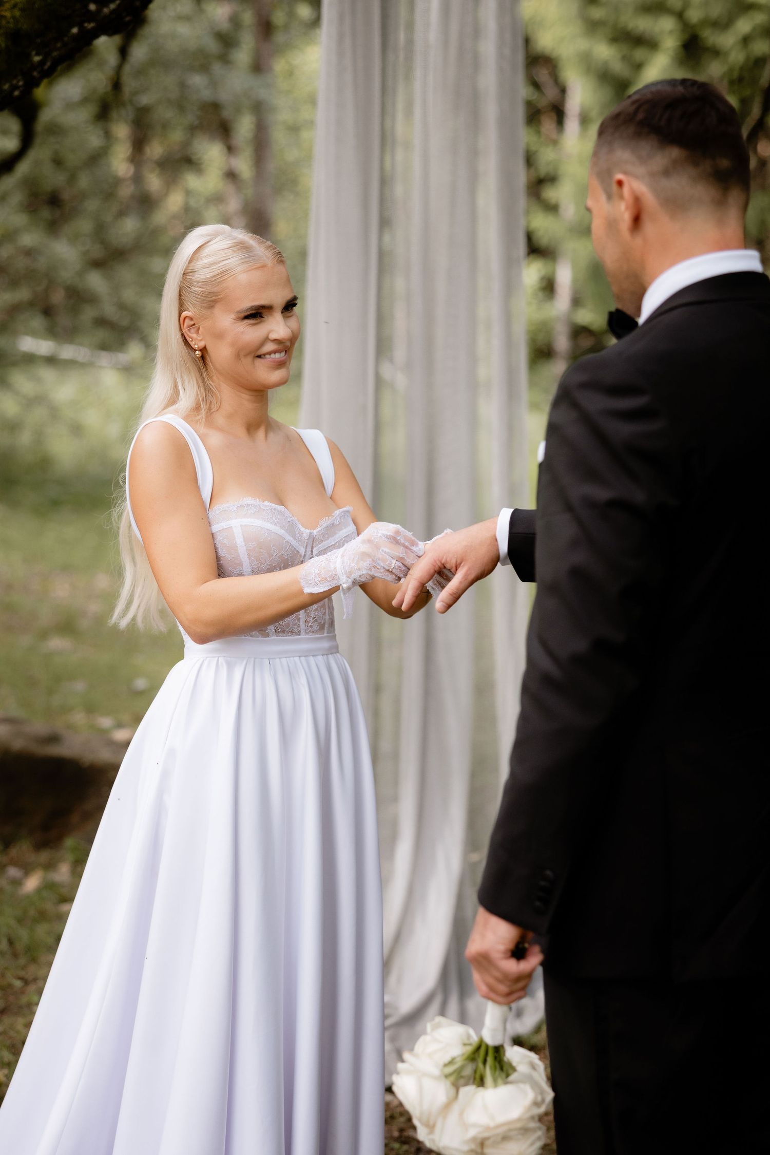 A wedding ceremony moment under white fabric draping and forest canopy.