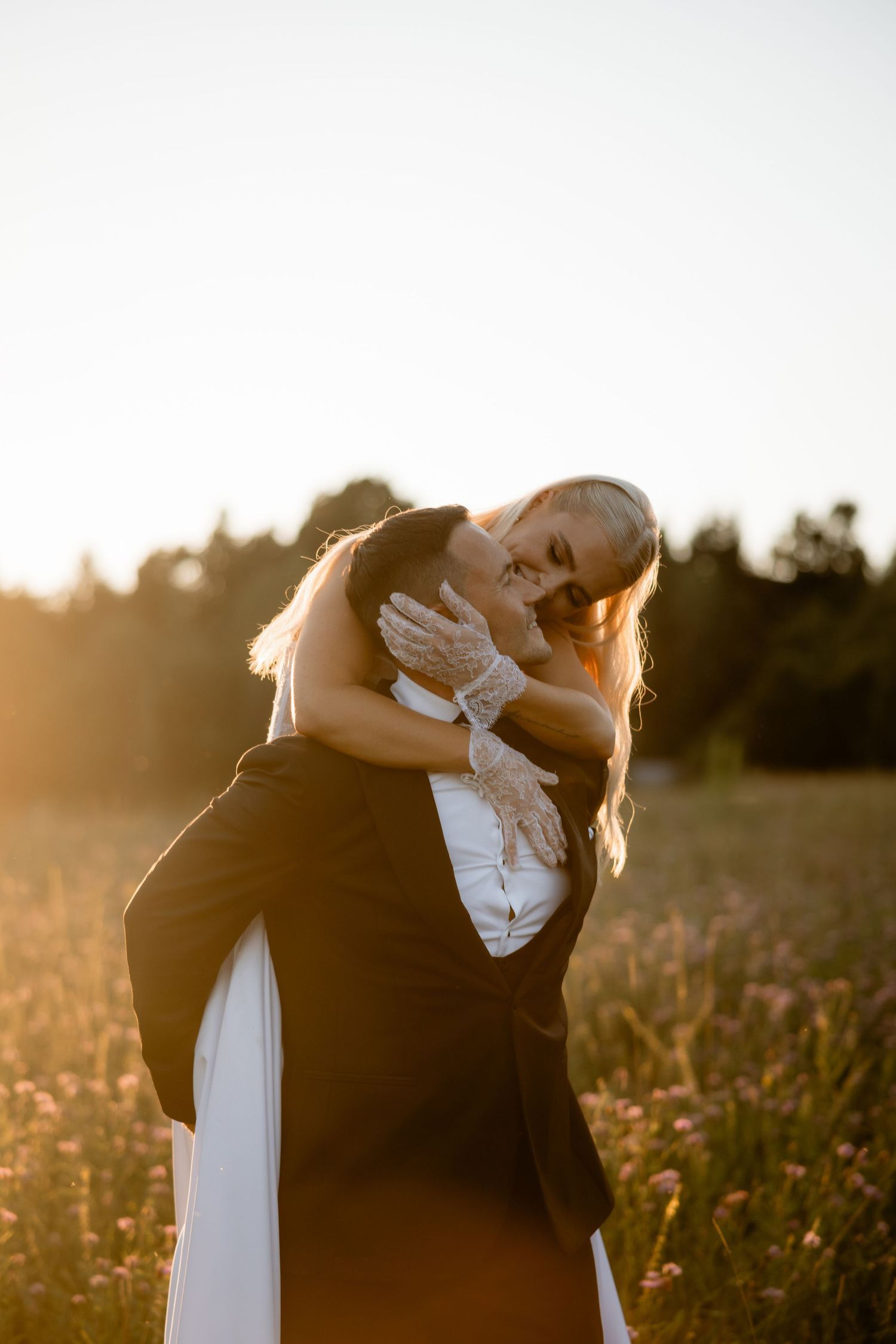 A romantic couple embraces in a sunset-lit wildflower field during their wedding photoshoot.