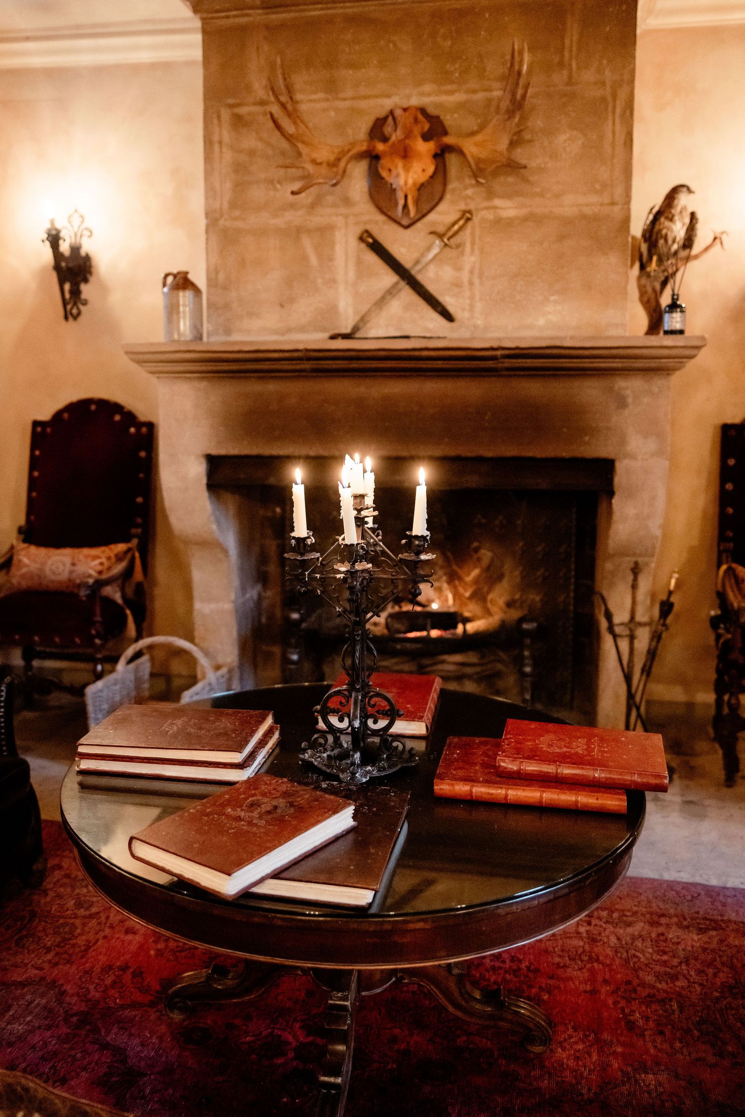 Medieval study displays an antique book on wooden desk with candlesticks and red carpet in a castle chamber setting.