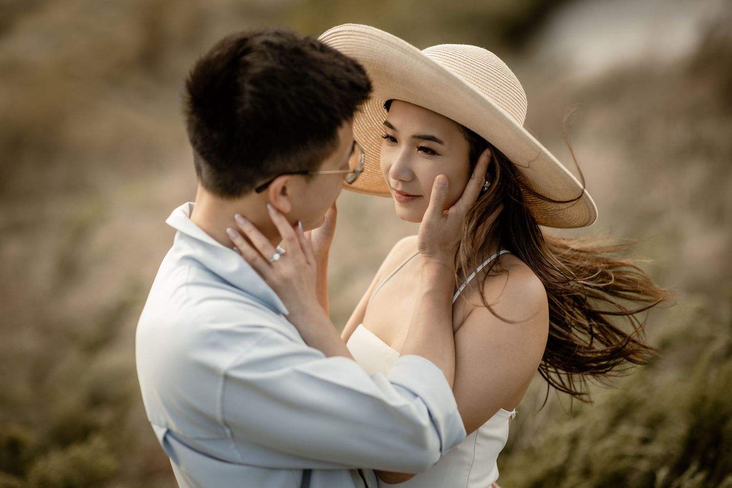 Romantic couple embraces in a dreamy outdoor photoshoot against golden sunlit hills.