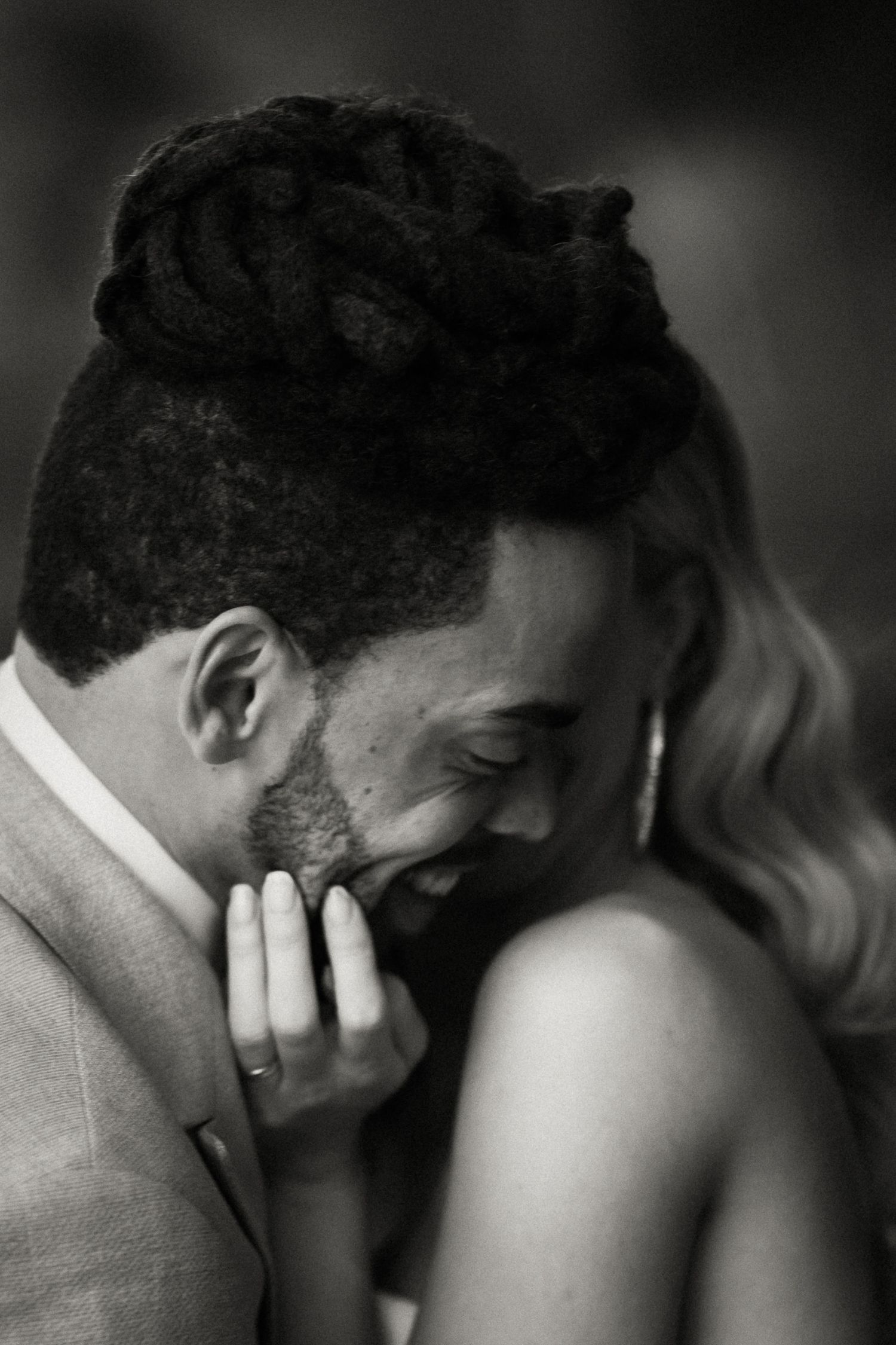 A couple shares an intimate black and white candid moment as they smile and embrace.