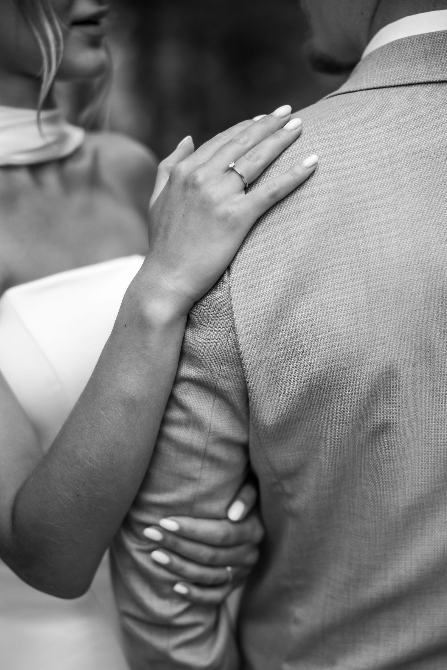 A tender black and white wedding photo showing hands with a ring embracing in an intimate moment.