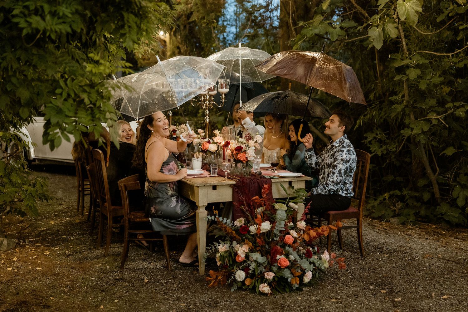 A romantic outdoor wedding ceremony setup with umbrellas and floral arrangements in a wooded garden setting.