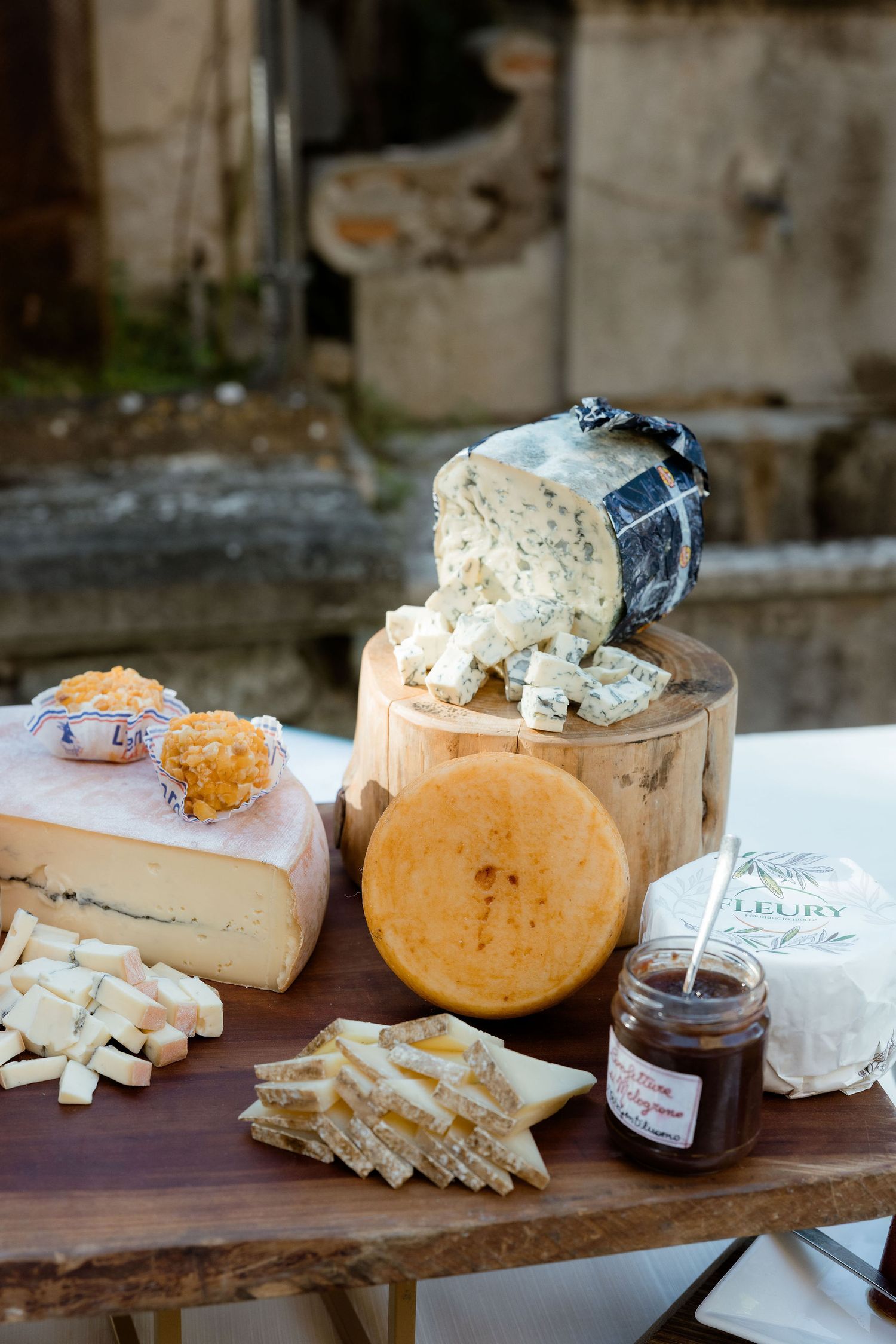 Artisanal cheese board display featuring various soft and hard cheeses with honey and preserves on a rustic wooden surface.