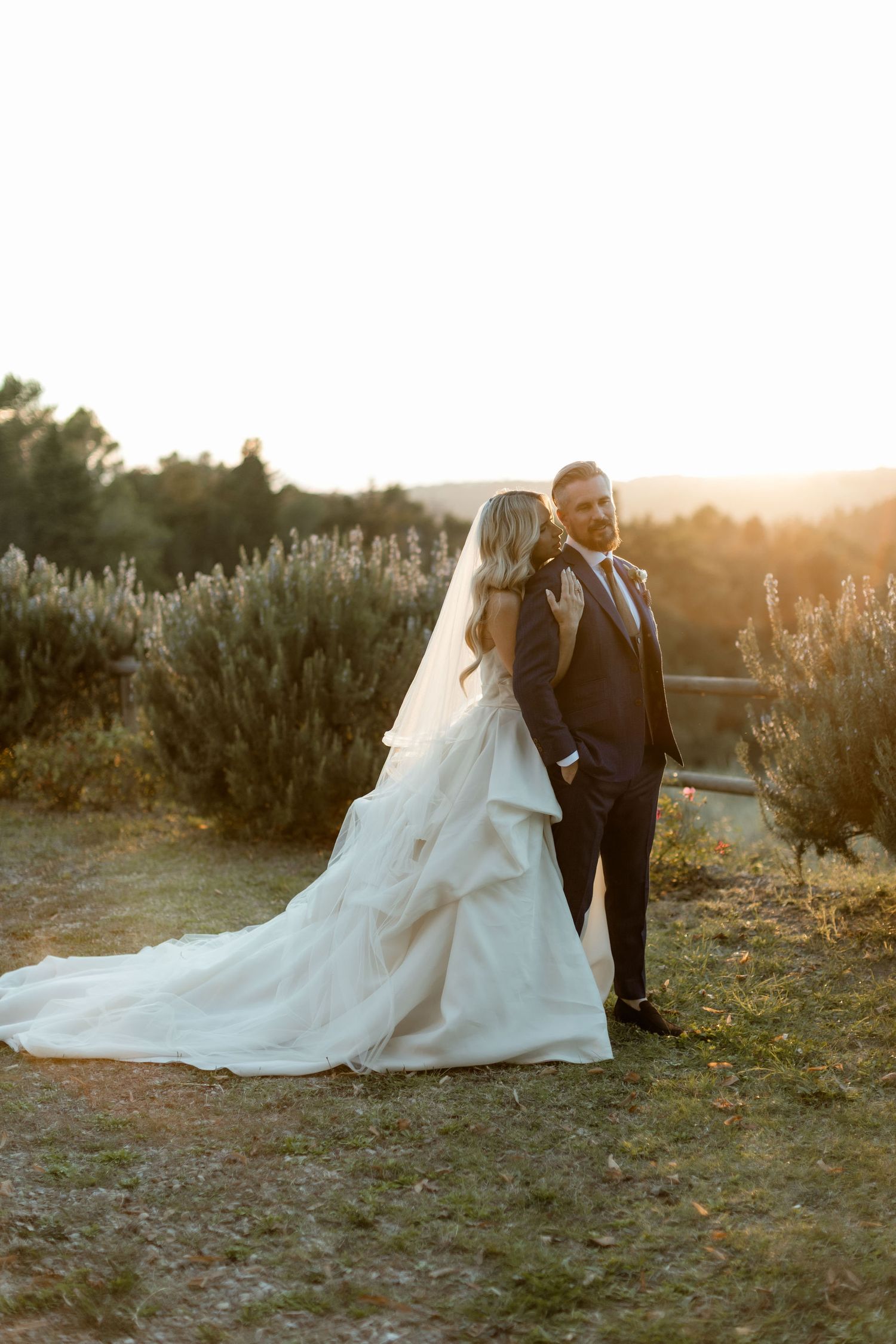 Romantic sunset wedding photos of couple in formal attire posing together in a rustic outdoor setting with golden light.