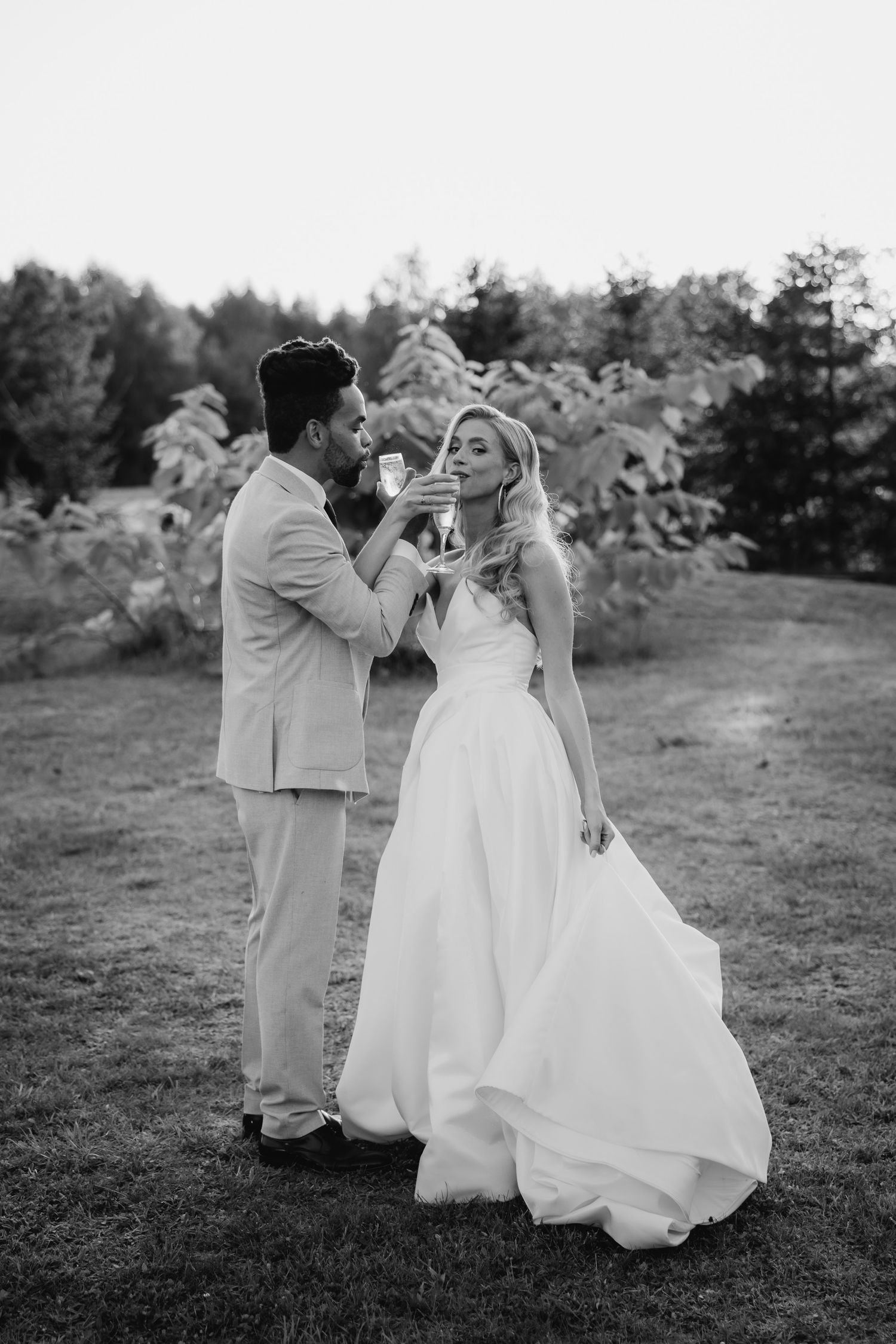 A black and white wedding photo showing a couple in a romantic moment outdoors with a flowing white dress and light suit.