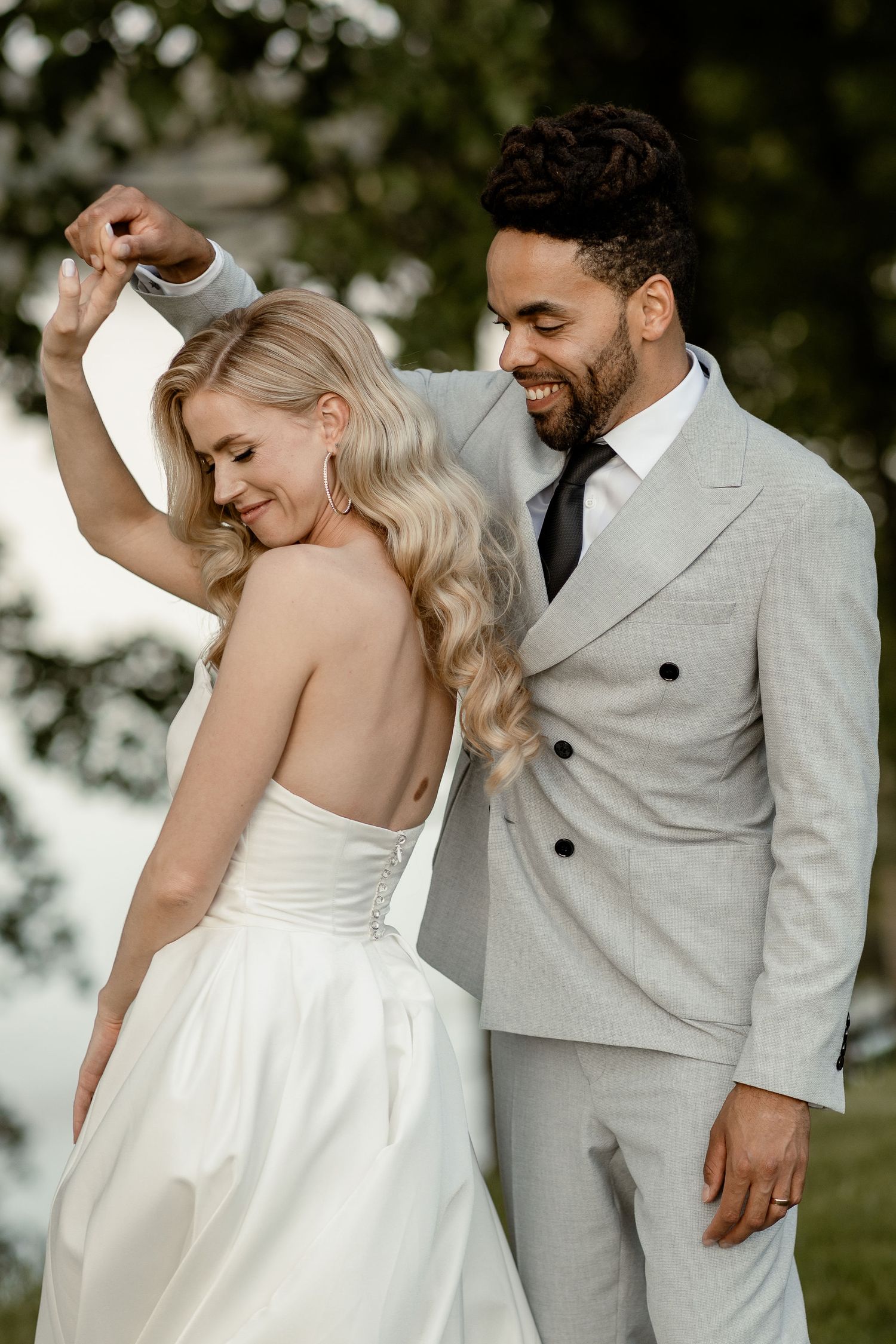 A couple shares a joyful moment together outdoors on their wedding day, with the bride in white and groom in light gray suit.