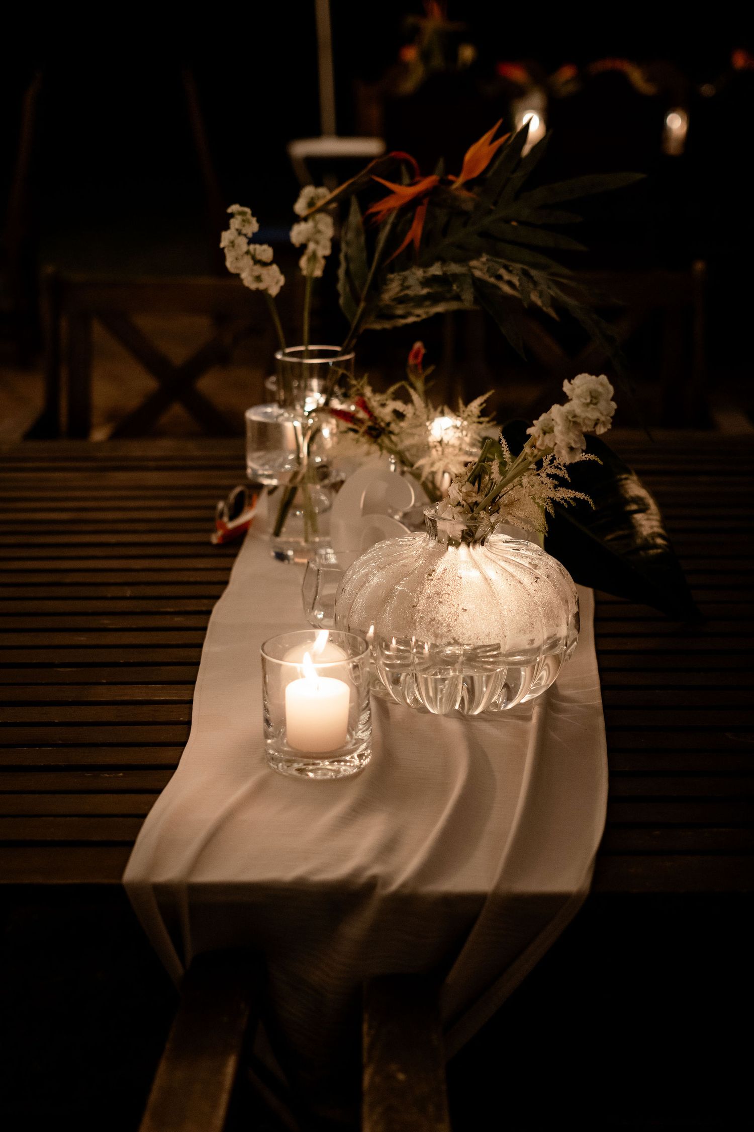 Elegant table setting with glowing candles, white pumpkin decor and floral arrangements on a cream-colored runner at night.