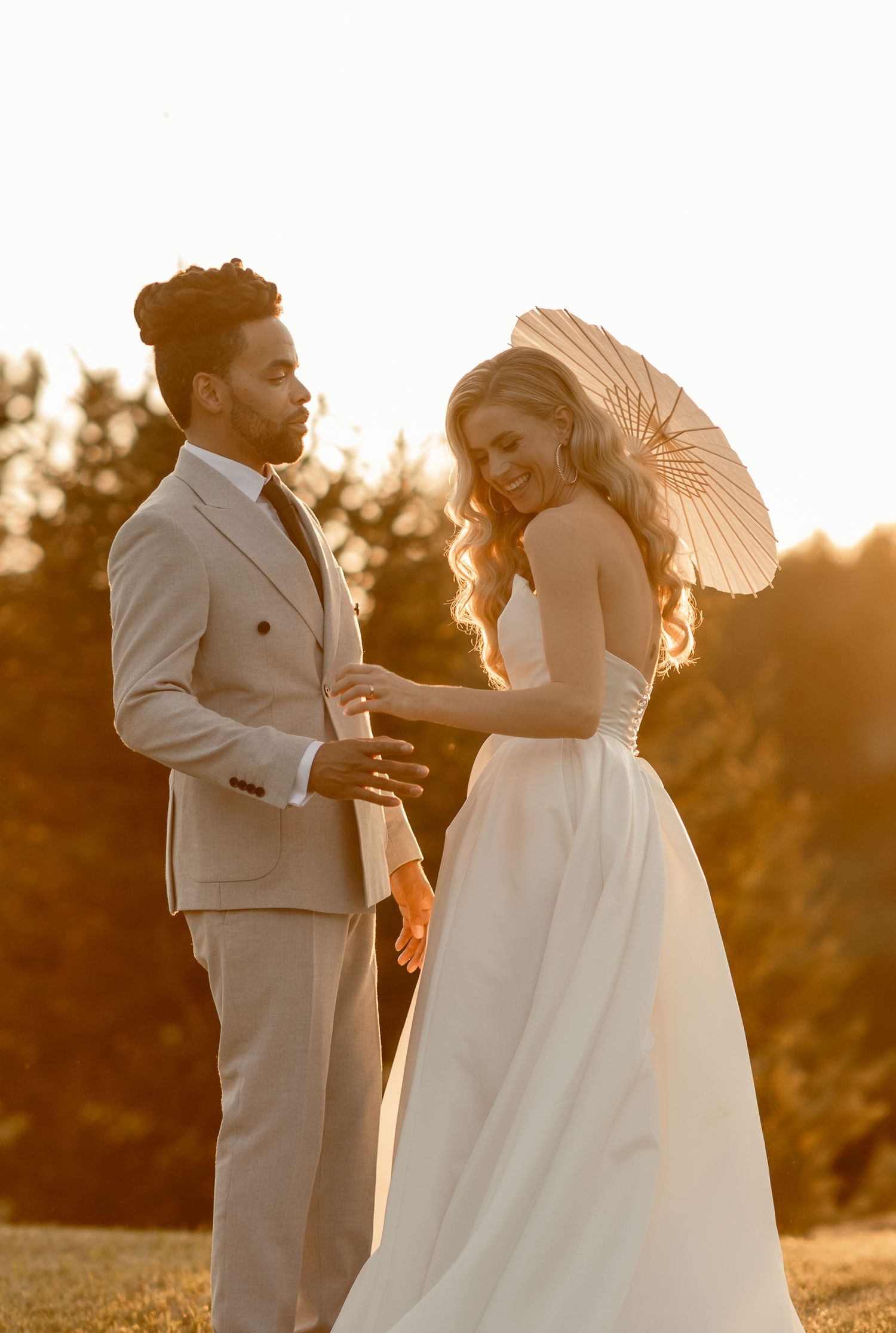 A couple shares a romantic moment at sunset with the bride holding a delicate parasol against the golden light.