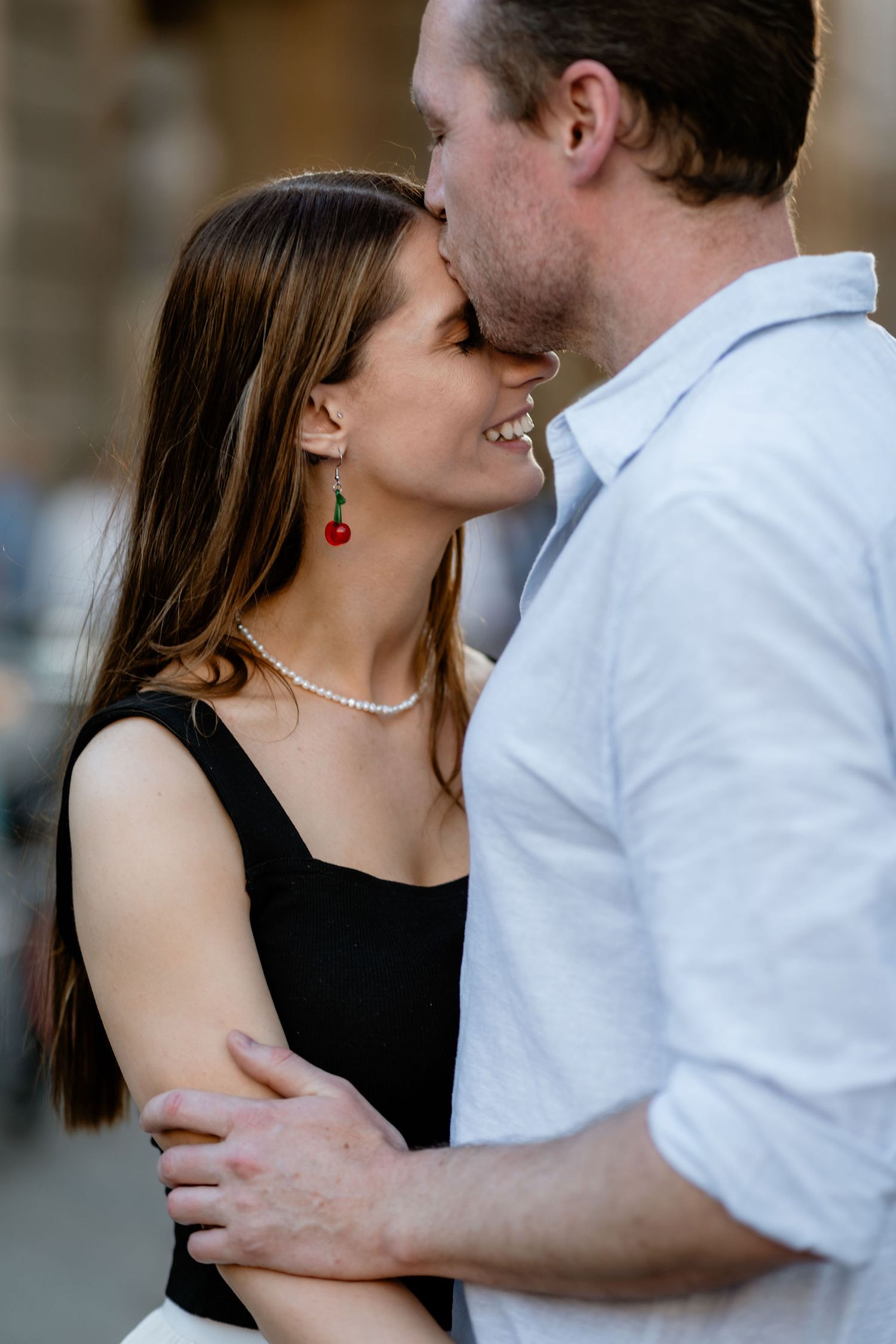 A romantic couple in an intimate embrace, with her wearing a black dress and pearls while he wears a white shirt.