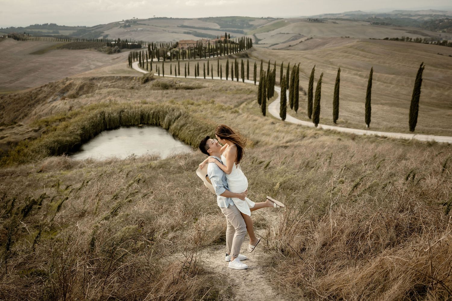 A romantic couple poses against a backdrop of Italian cypress trees in Tuscany.