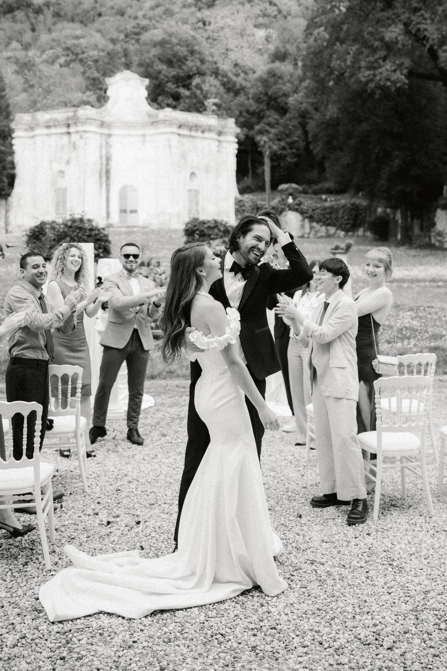 Joyful wedding celebration outdoors with people dancing and celebrating in front of a historic stone structure.