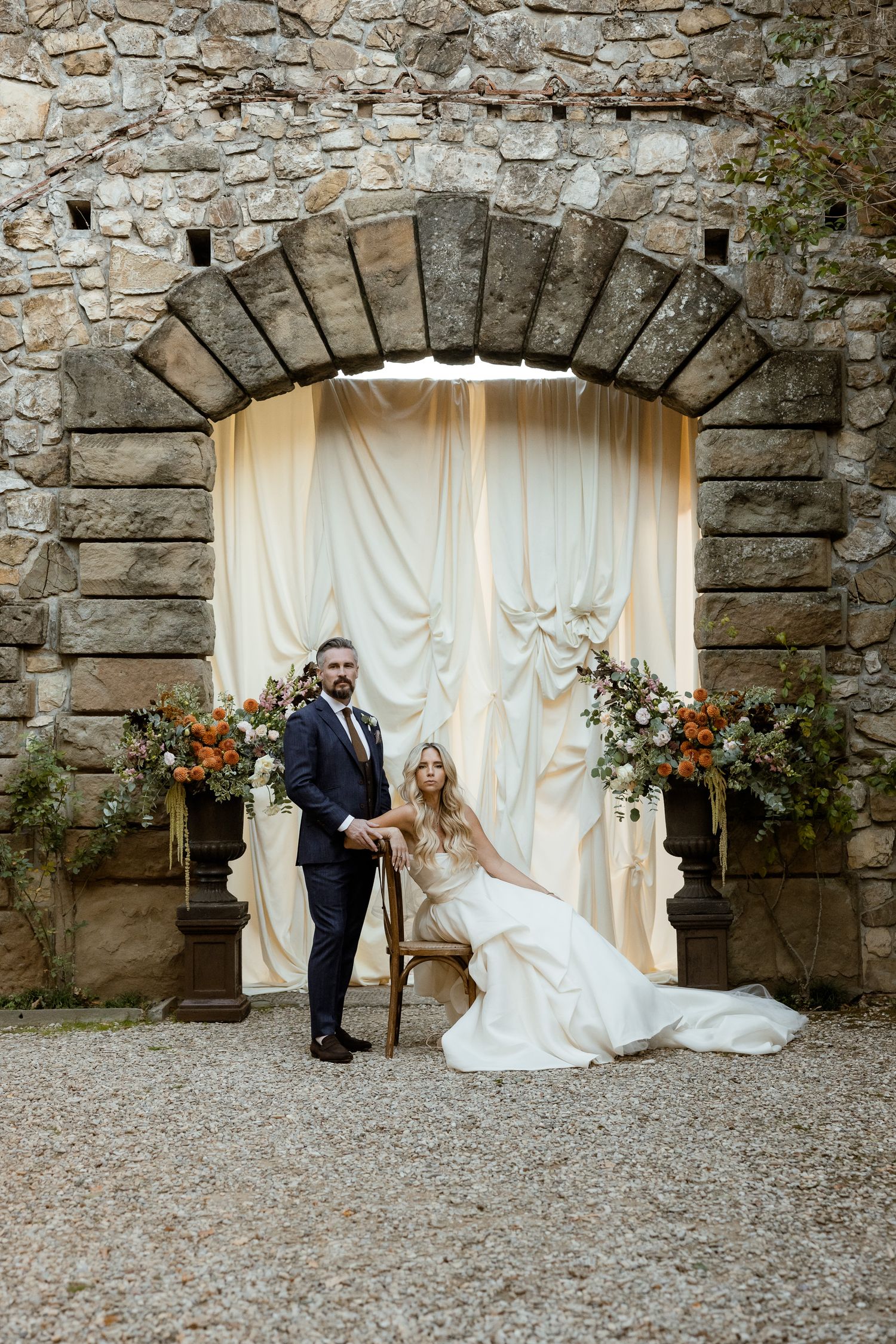 A romantic wedding photo series against a rustic stone wall with white curtains and floral arrangements.