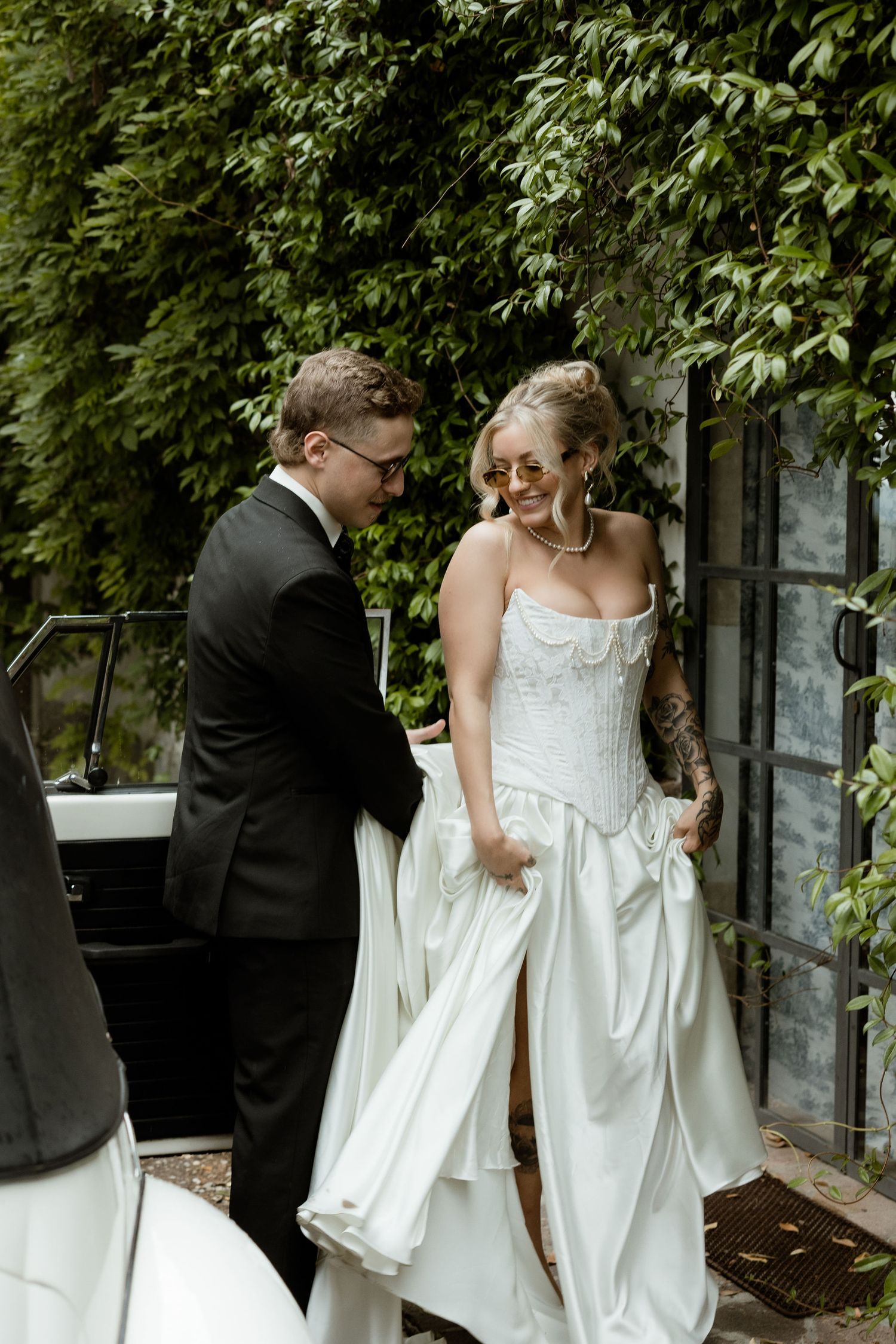 A joyful wedding moment captured in a garden setting with a white bridal gown and black tuxedo.