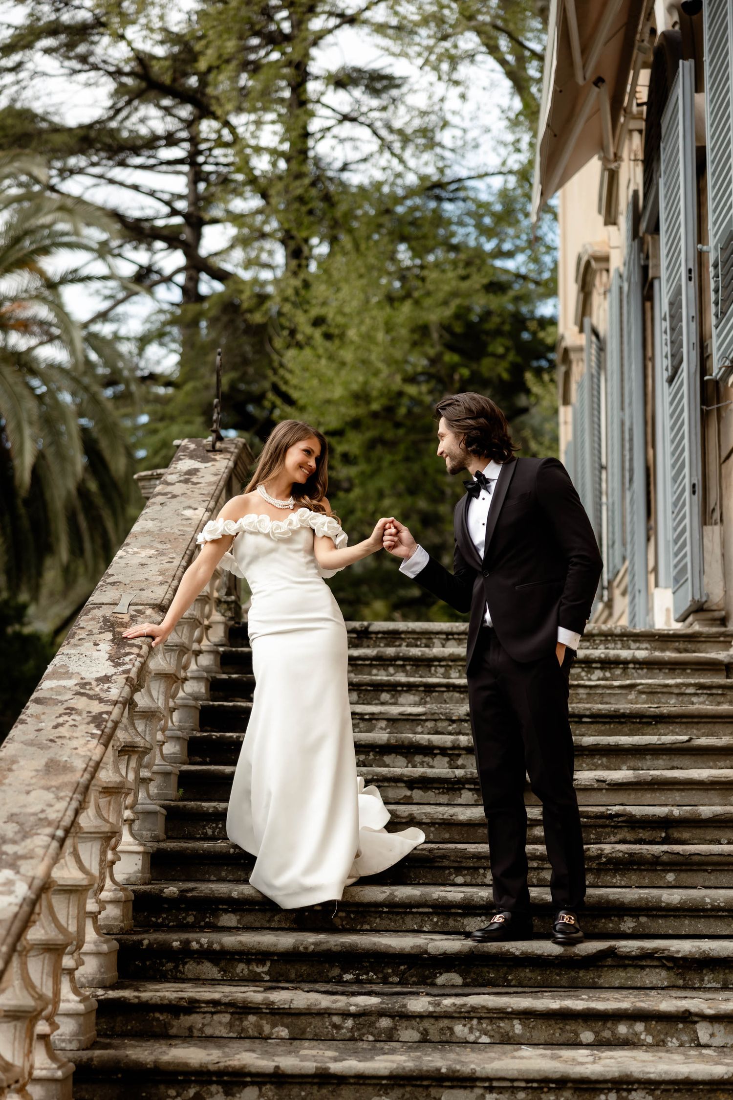 A couple in wedding attire dancing and twirling on historic stone steps surrounded by trees.