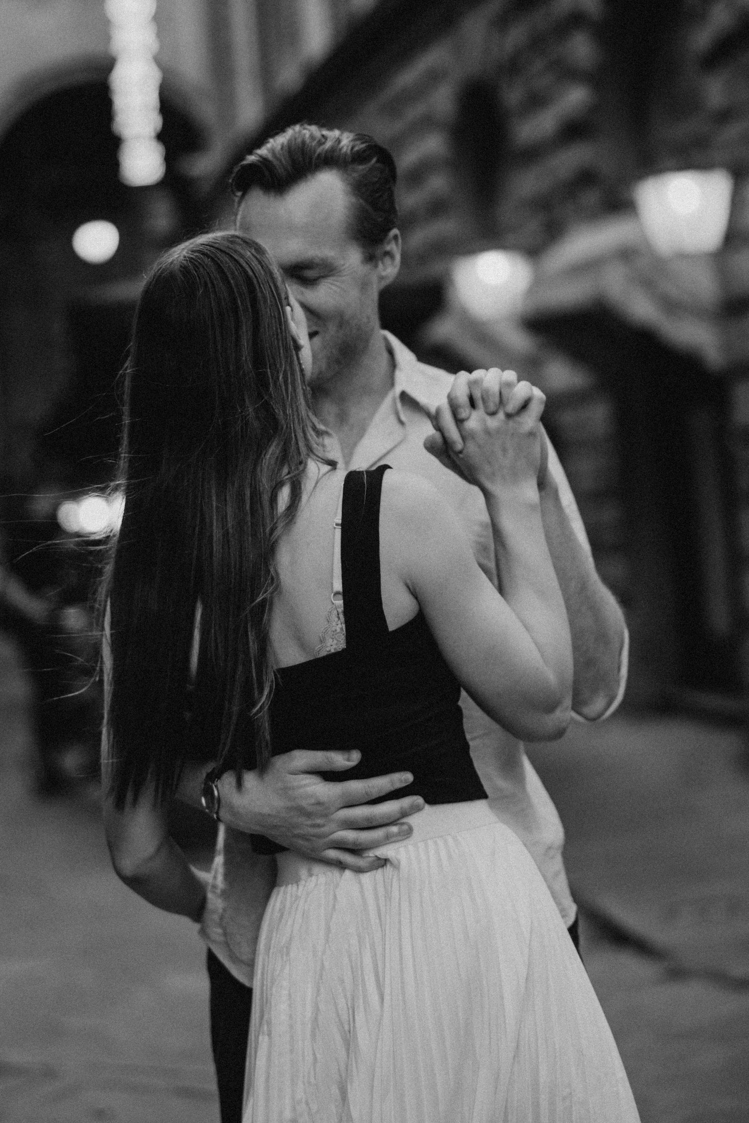 A romantic black and white photo of a couple dancing together on a city street at night.