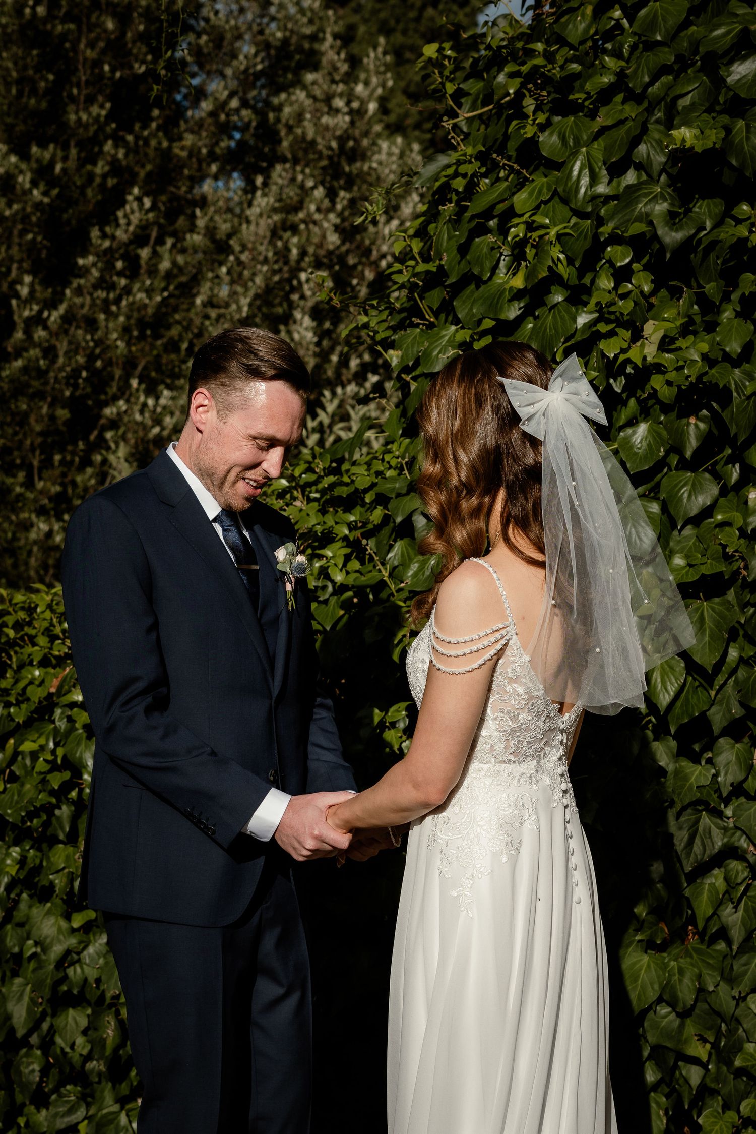 A couple shares an intimate moment during their wedding ceremony in a garden setting with lush greenery.
