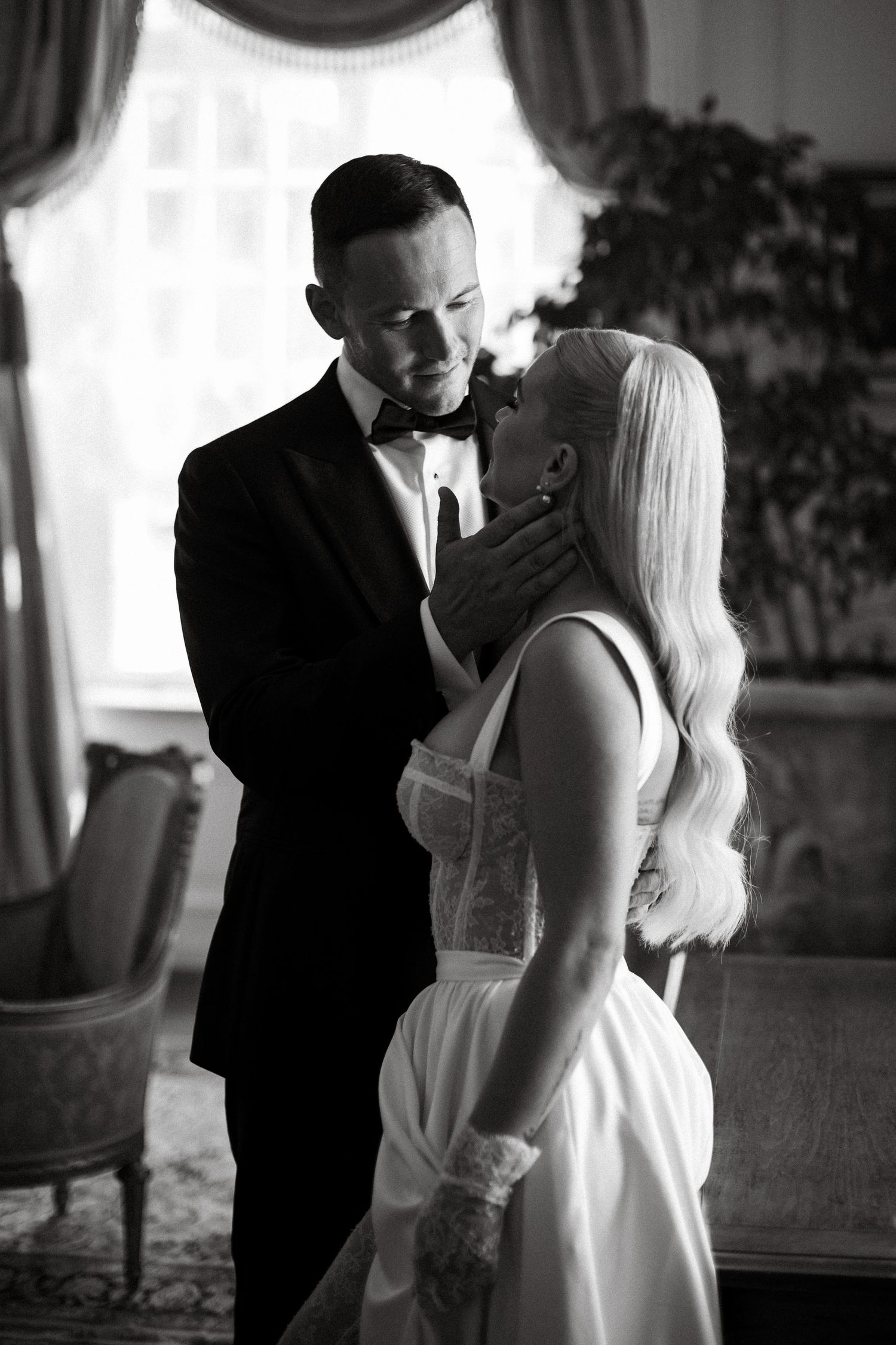 Intimate black and white portrait of couple sharing tender moment in formal setting.