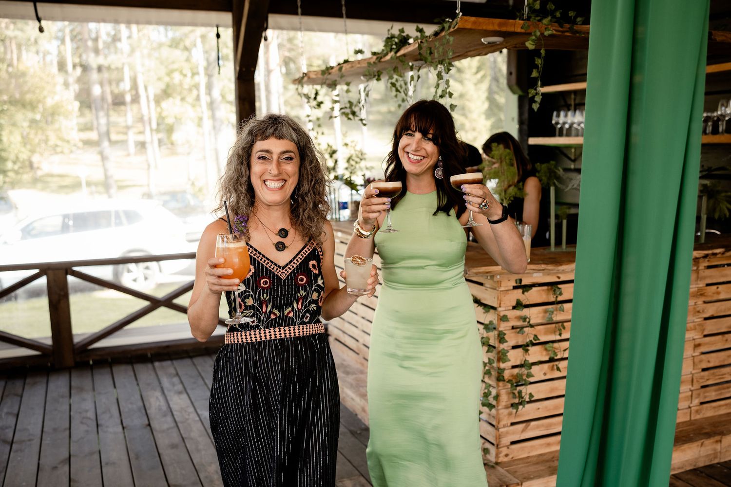 Two guests raise champagne glasses on an outdoor porch during a celebration.
