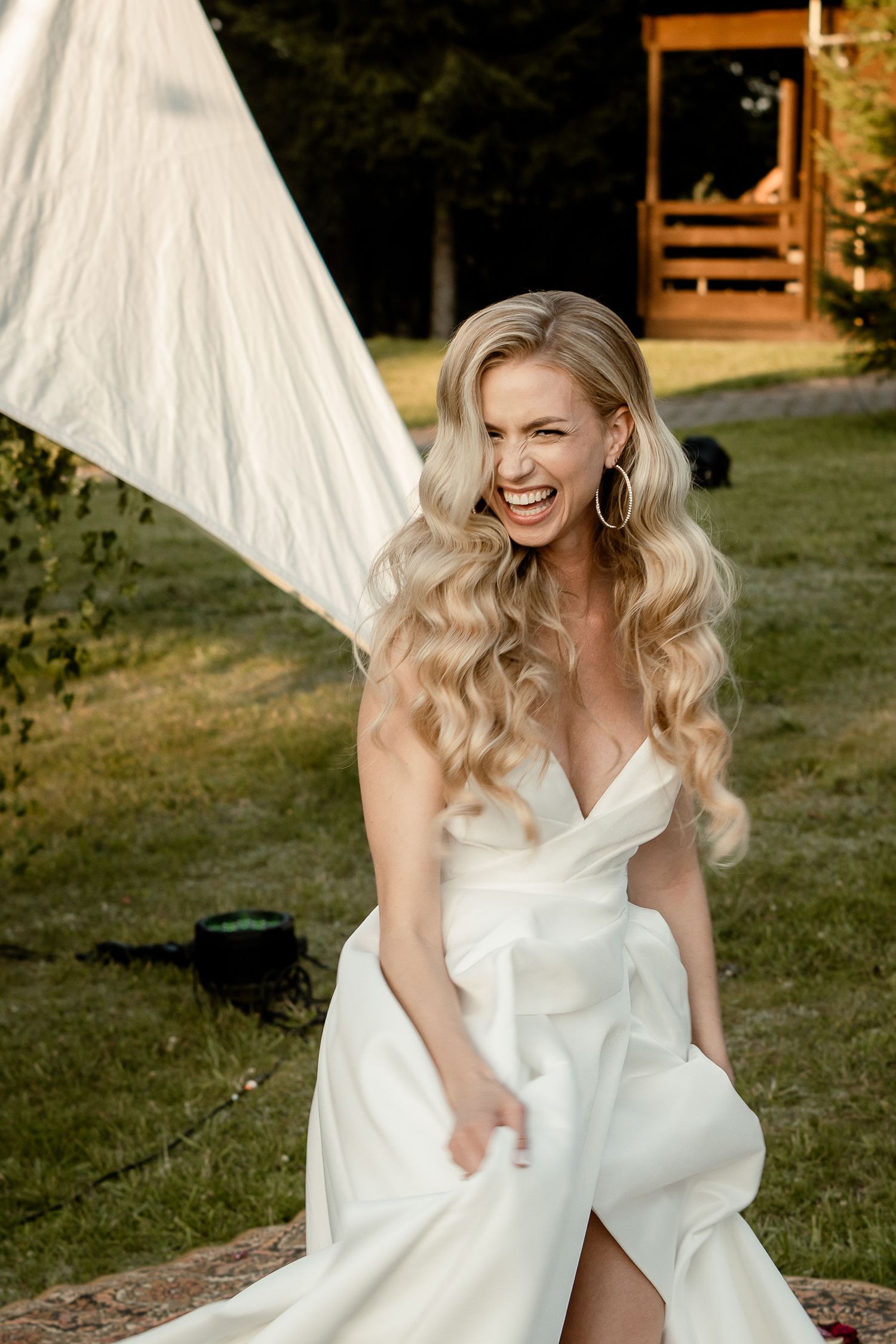Bride in elegant white wedding dress poses outdoors with joyful expression.