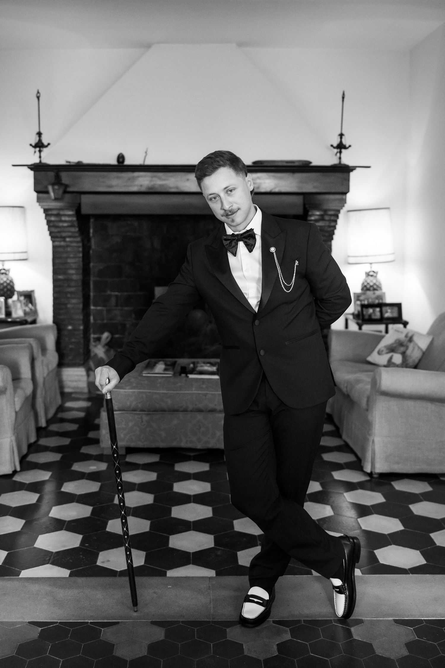 A person in formal attire performs dance moves on a black and white checkered floor.