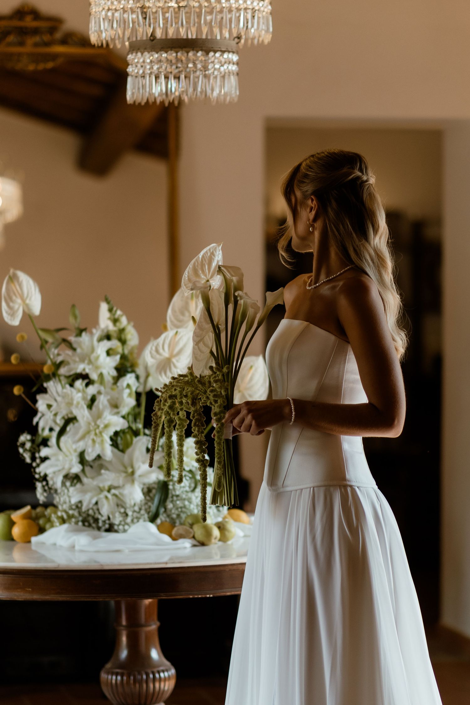 A series of elegant white floral arrangements with crystal chandeliers decorating a rustic indoor wedding venue.