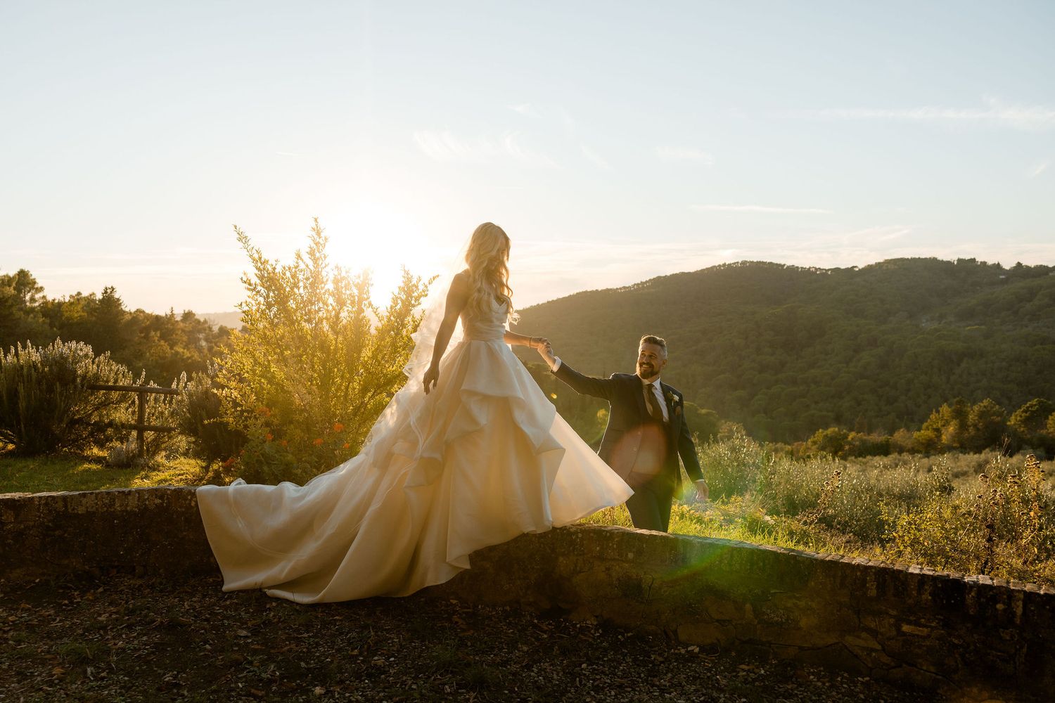 Couple in wedding attire walking through scenic mountain landscape at golden sunset.