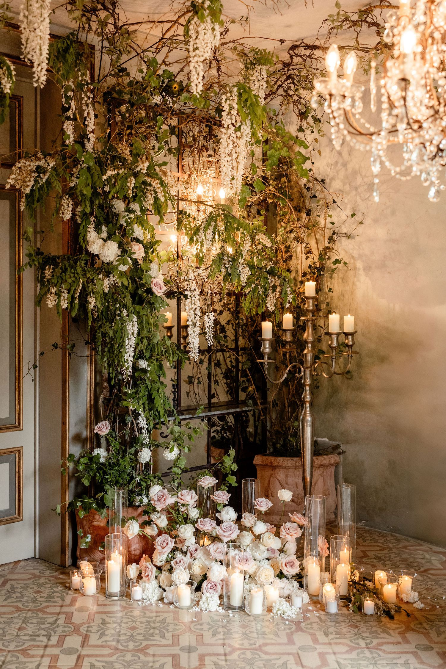 Elegant wedding venue entrance decorated with cascading greenery, white roses and glowing candles in glass holders.
