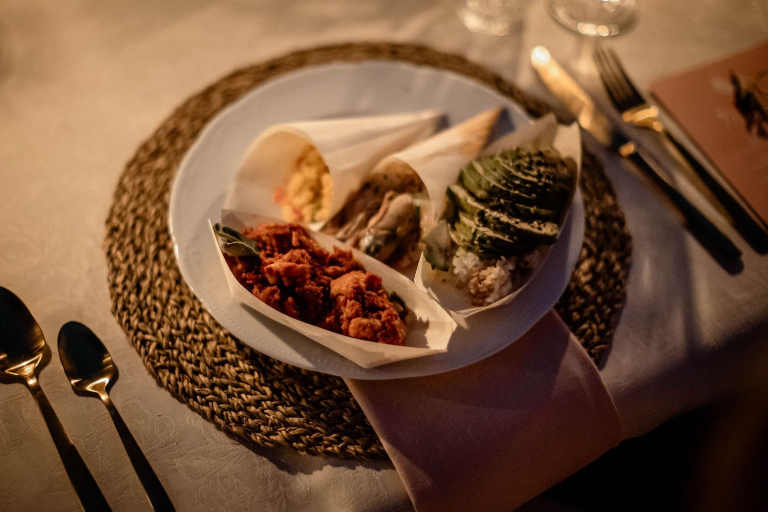 Elegant plated dinner setting with food on woven placemat at wedding reception.