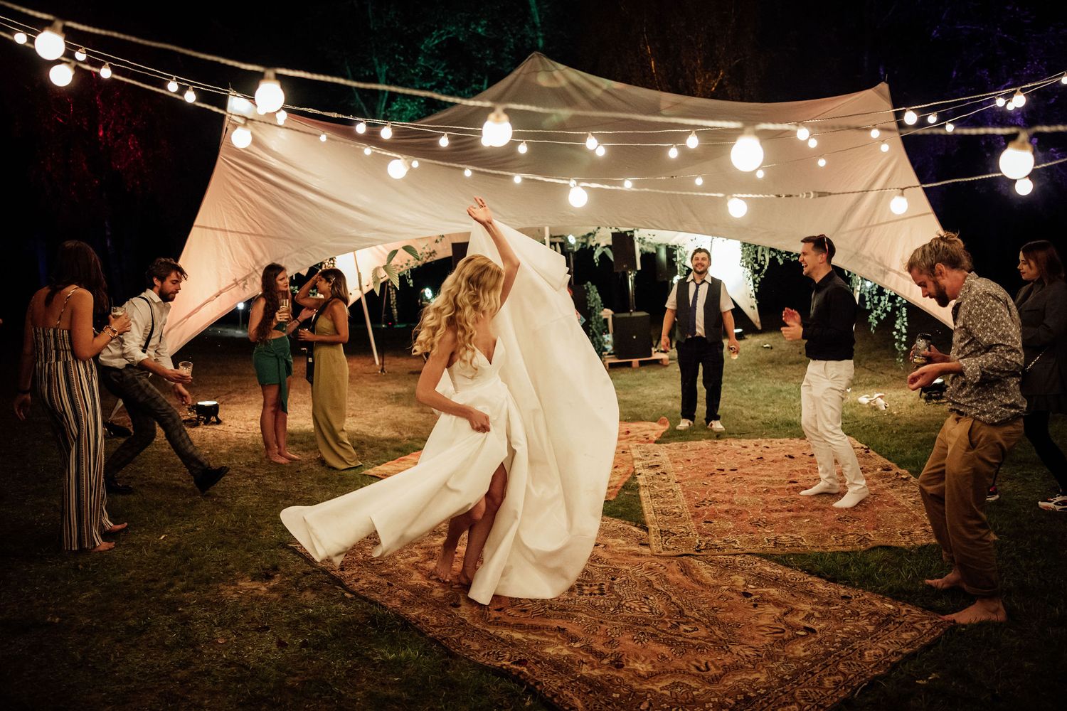 People dancing at a nighttime outdoor wedding reception under string lights and a white canopy tent.