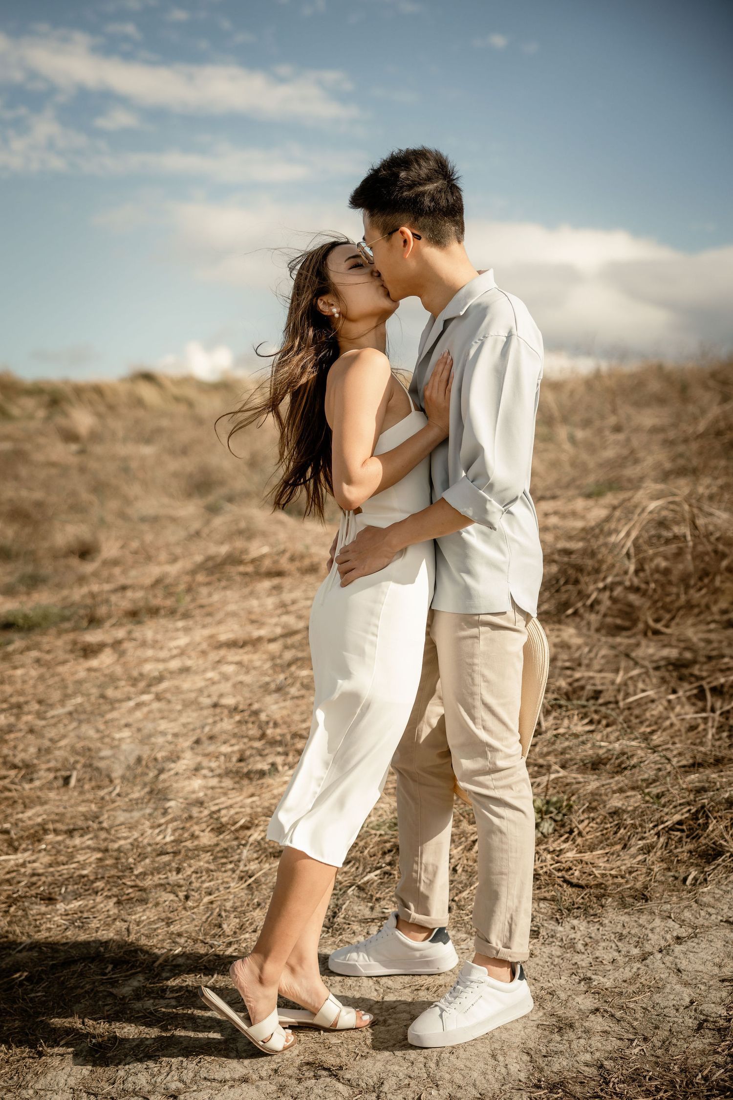 An intimate embrace captured against golden hills and blue sky in matching light summer attire.