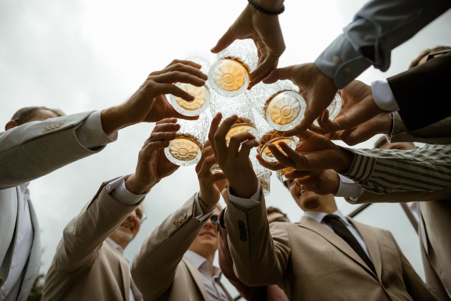 Group of hands reaching up to toast and clink beer glasses together in celebration from below perspective.