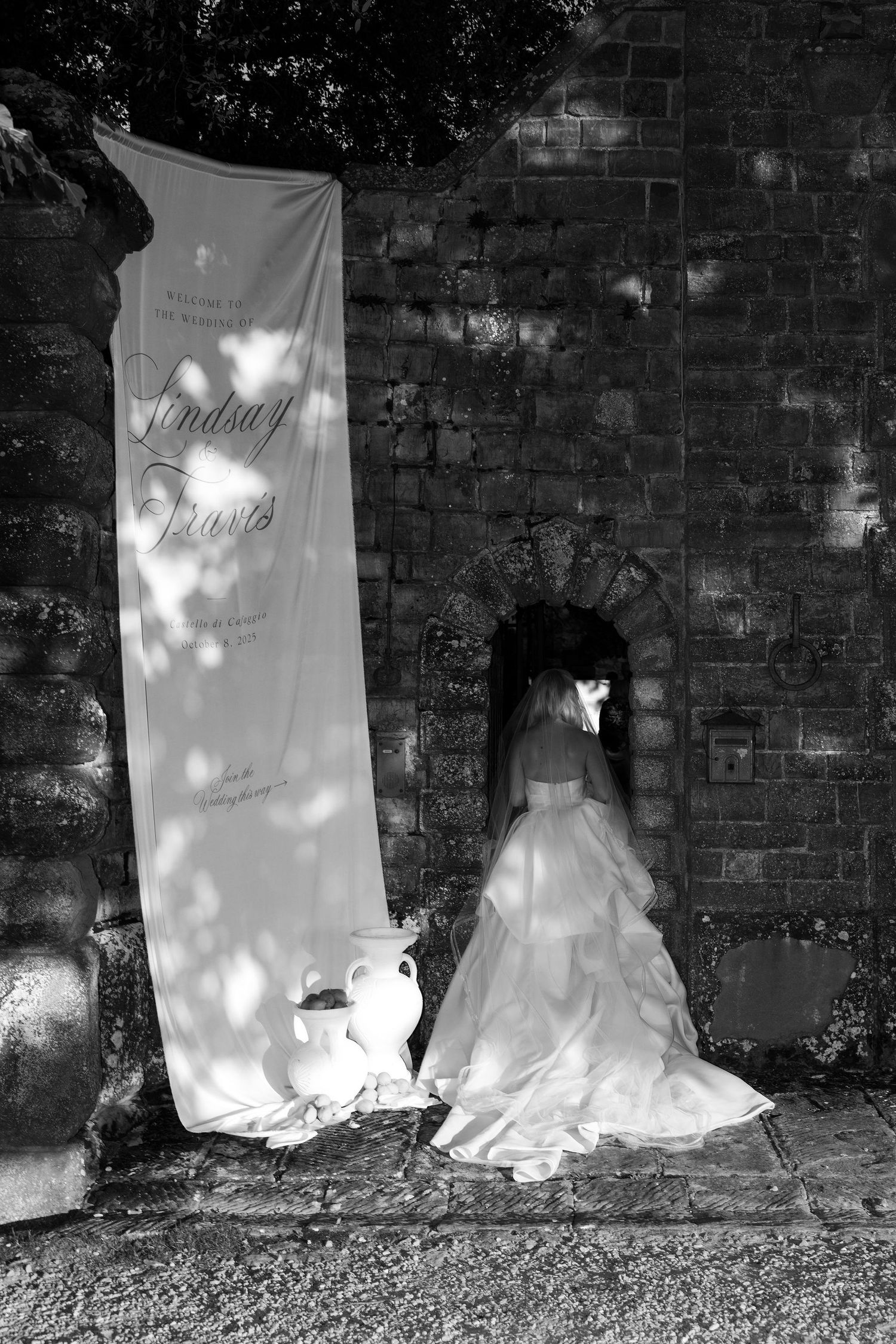 A series of white wedding dresses displayed against a dark brick wall with dramatic lighting creating shadow patterns.