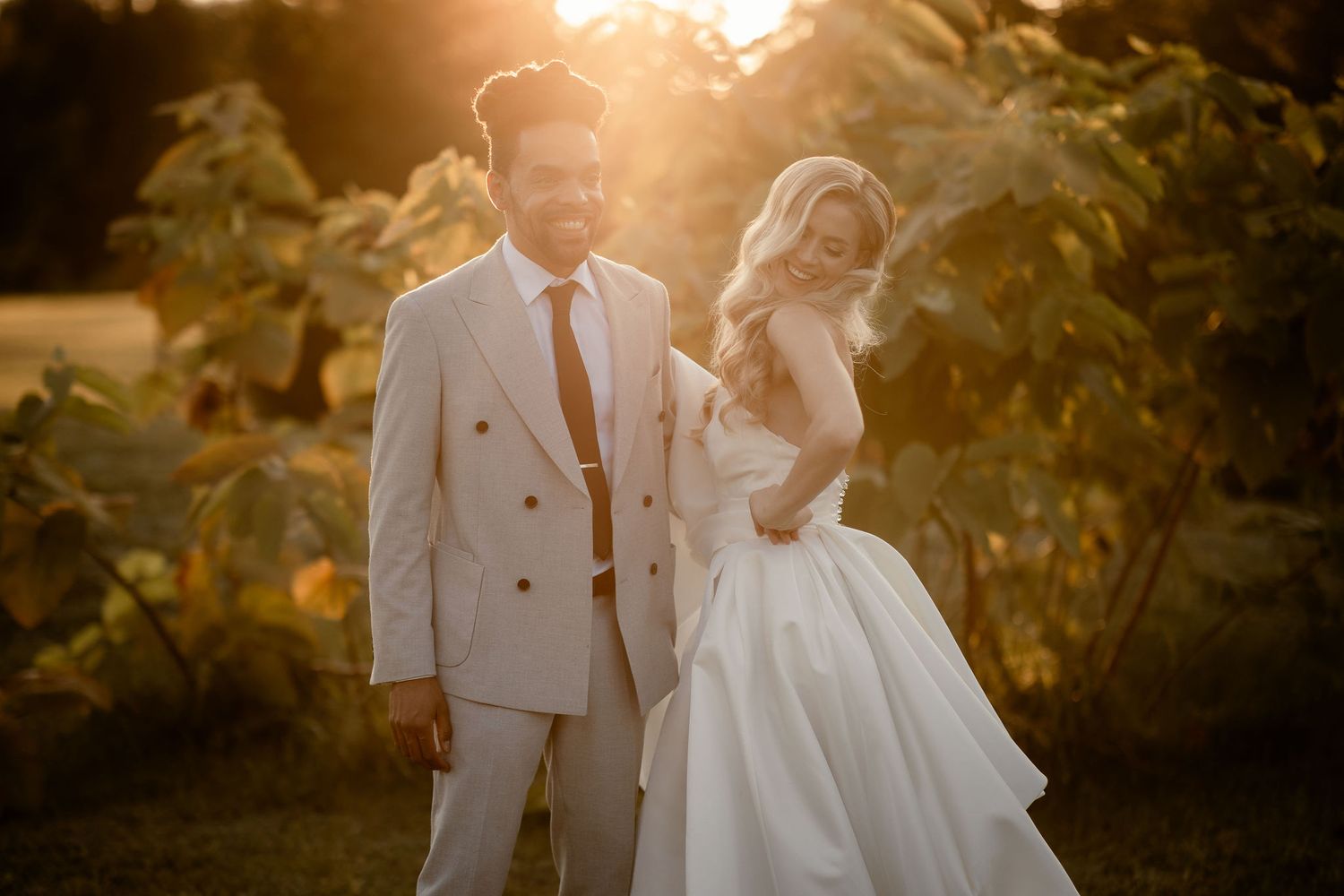 Stylish wedding couple stands together during sunset in a lush garden setting.