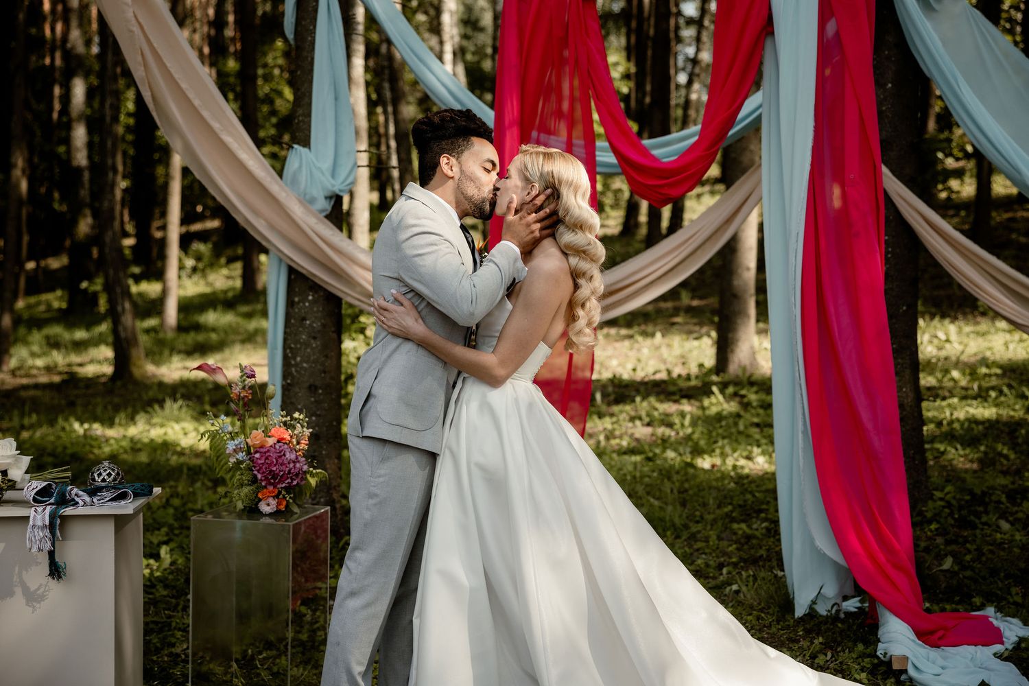Romantic forest wedding ceremony with elegant fabric draping and floral arrangements in natural setting.