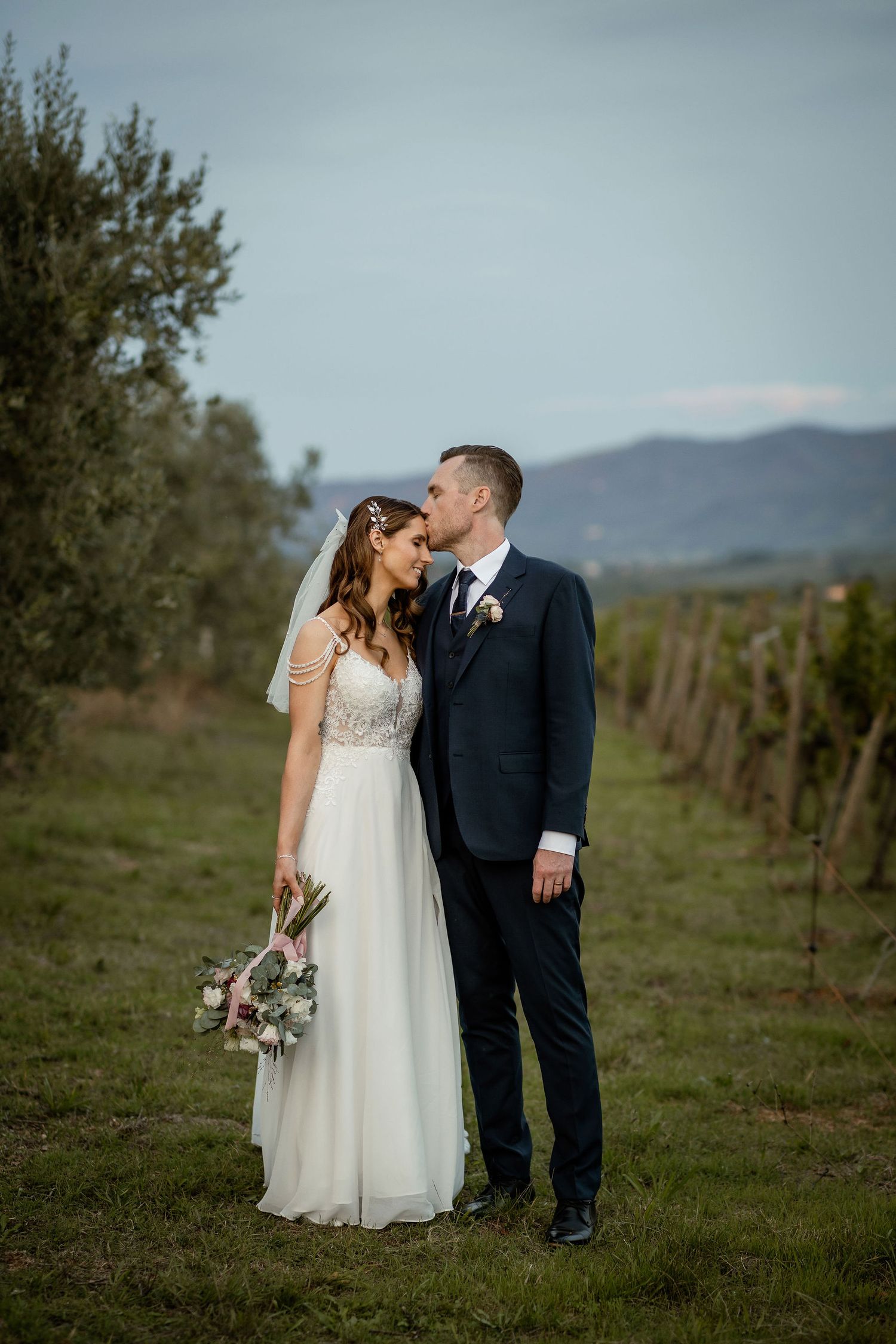 Romantic wedding portrait in a vineyard with mountains in the background during golden hour.