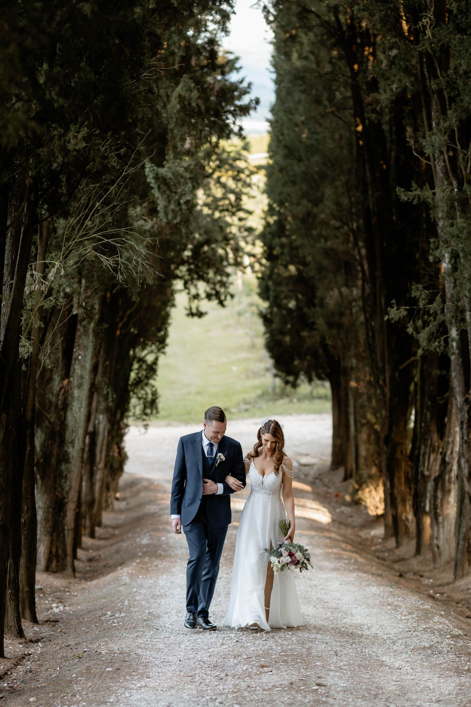 Newlyweds walking together down a cypress-lined path in an Italian garden setting.