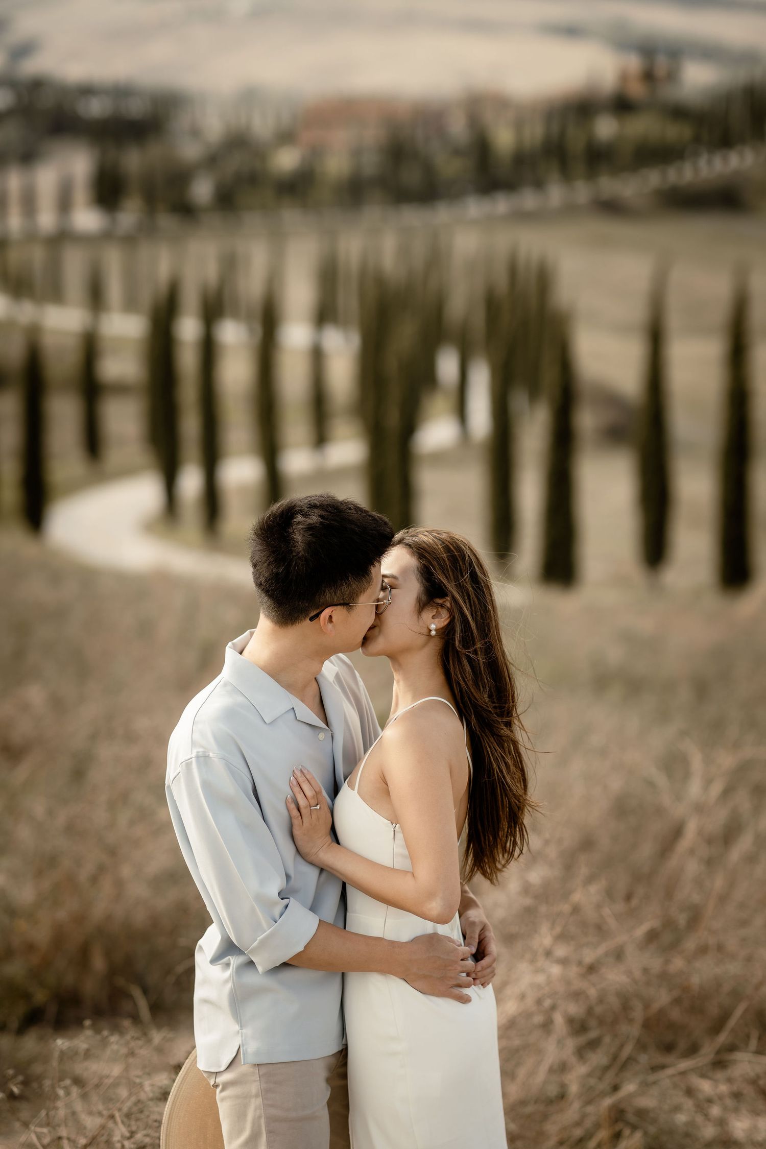 Romantic couple embracing in a scenic Tuscan landscape with cypress trees.