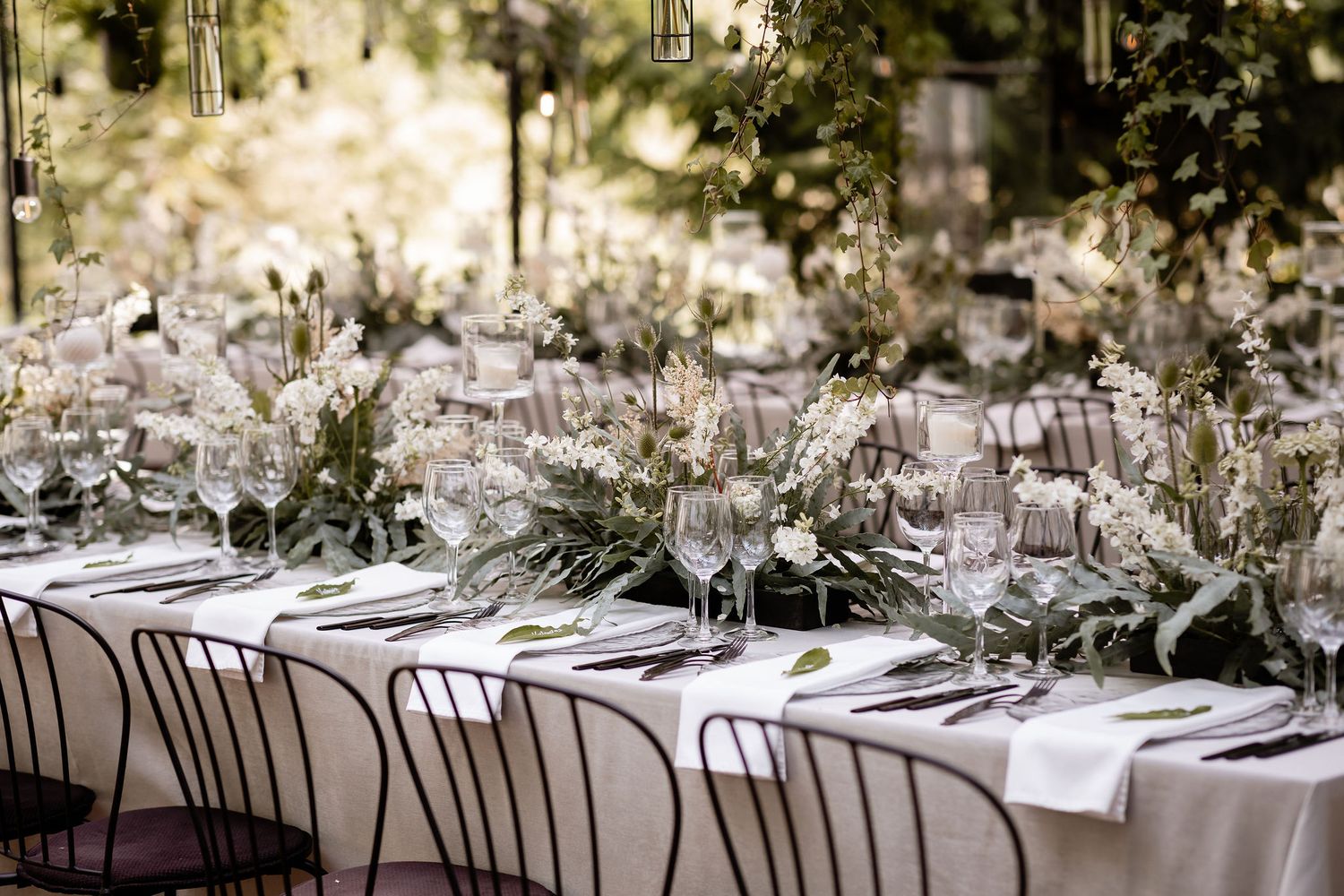 Elegant wedding table setting with delicate floral arrangements and white linens in an outdoor garden setting.