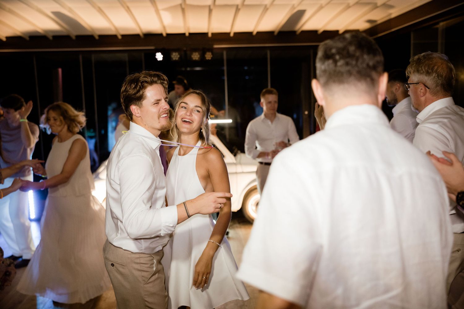 Wedding guests dance and celebrate together on a dimly lit dance floor during an evening reception.