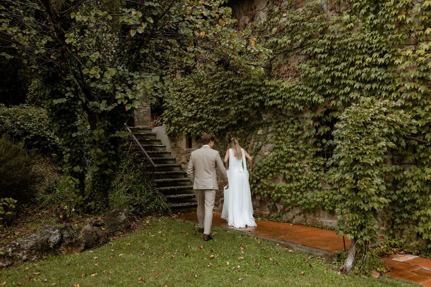 A couple walks through a lush garden pathway with stone steps and greenery creating a romantic outdoor setting.