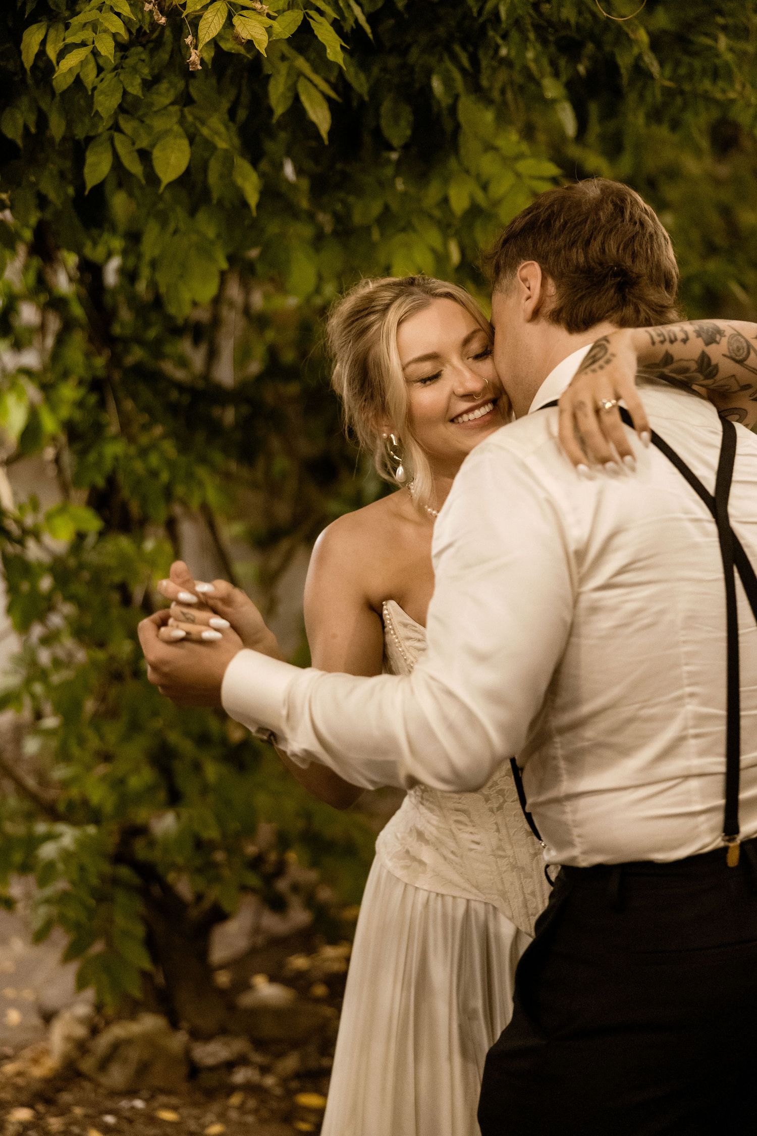 A romantic sequence of embraces between a couple in formal attire under green leaves during golden hour.
