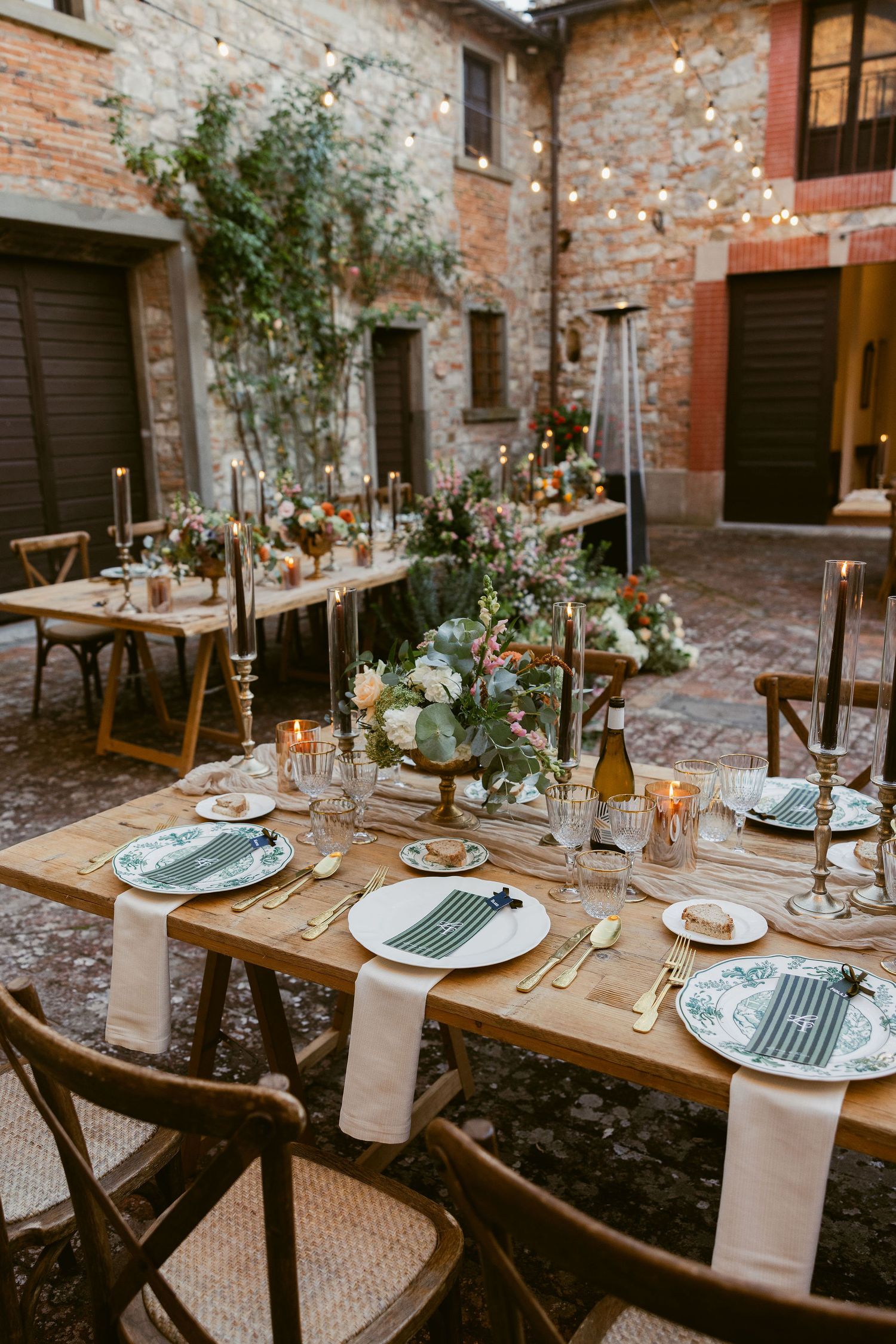 Rustic outdoor wedding reception tables set with blue plates and floral centerpieces in a charming brick courtyard.