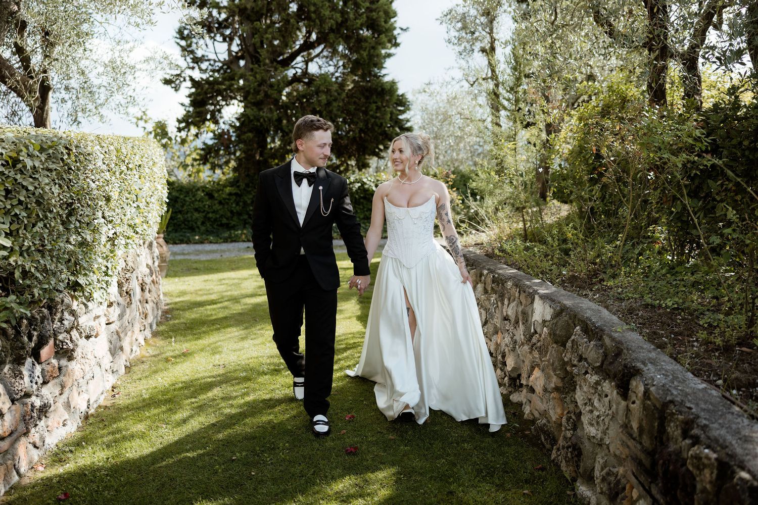 A couple walks together on a scenic path through lush gardens during a formal wedding celebration.