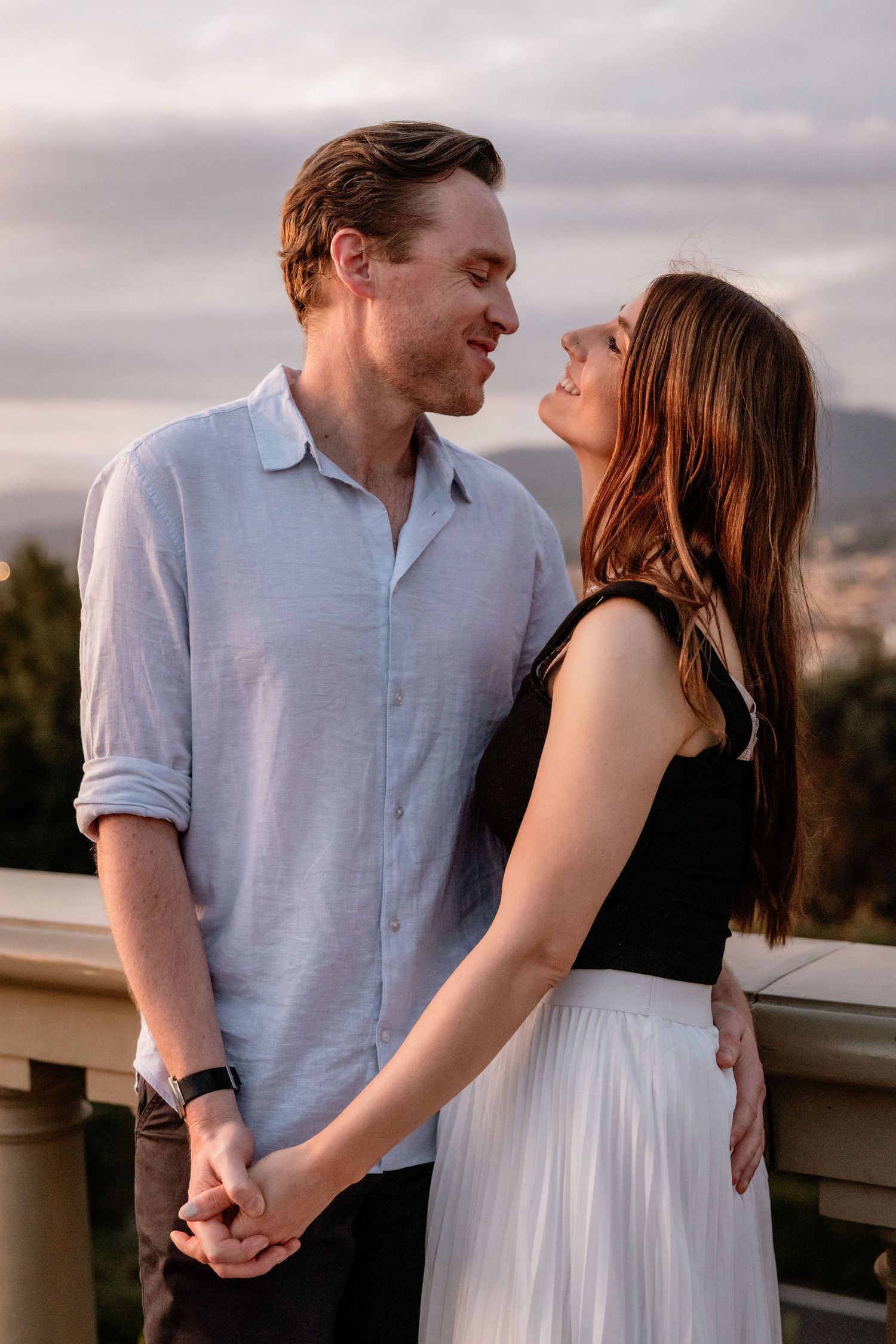 A couple gazes lovingly at each other while holding hands during golden hour on an outdoor terrace.