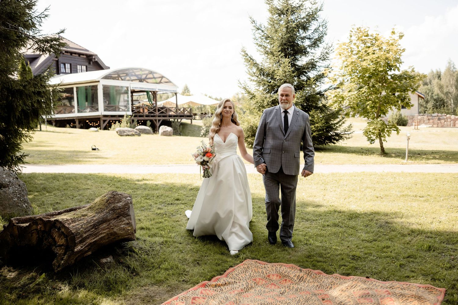 Newlyweds walk across lawn with house and gazebo in background.