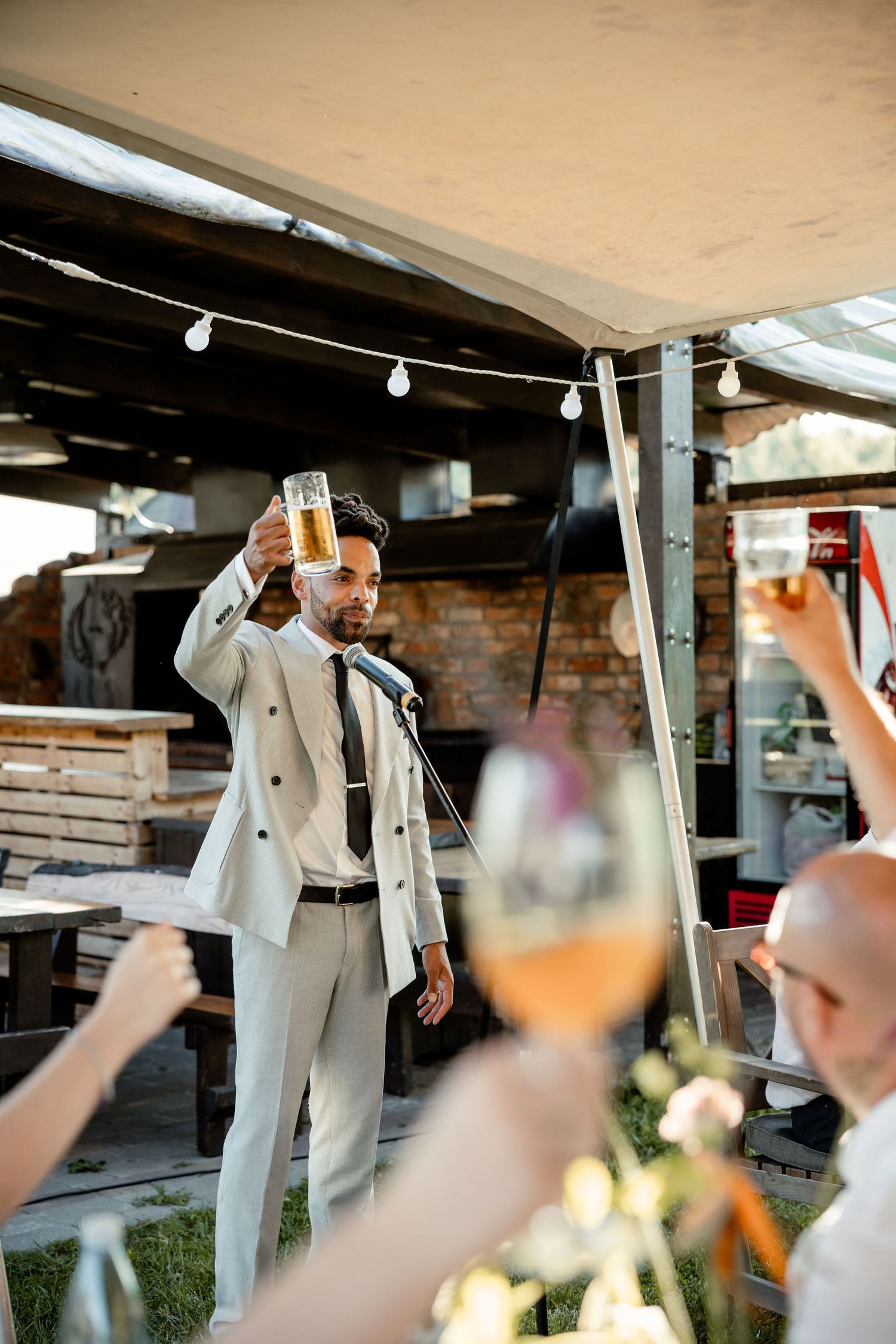 A celebratory toast at an outdoor wedding reception under string lights with guests raising glasses.