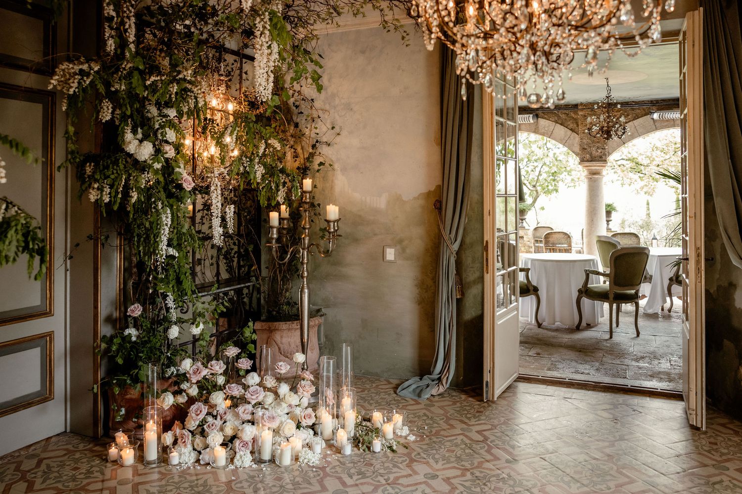 Elegant wedding venue entrance with crystal chandelier, cascading greenery, and romantic candlelit floor display.